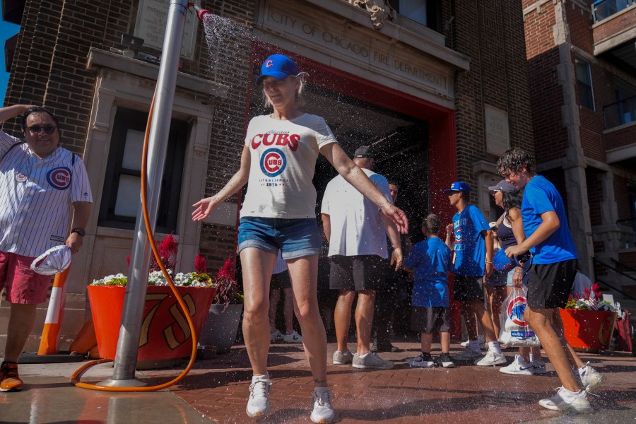 Baseball fans cool off under a sprinkler provided by the Chicago Fire Department outside of Wrigley Field after a hot baseball game between the Seattle Mariners and Chicago Cubs, Saturday, June 21, 2025, in Chicago. (AP Photo/Erin Hooley)