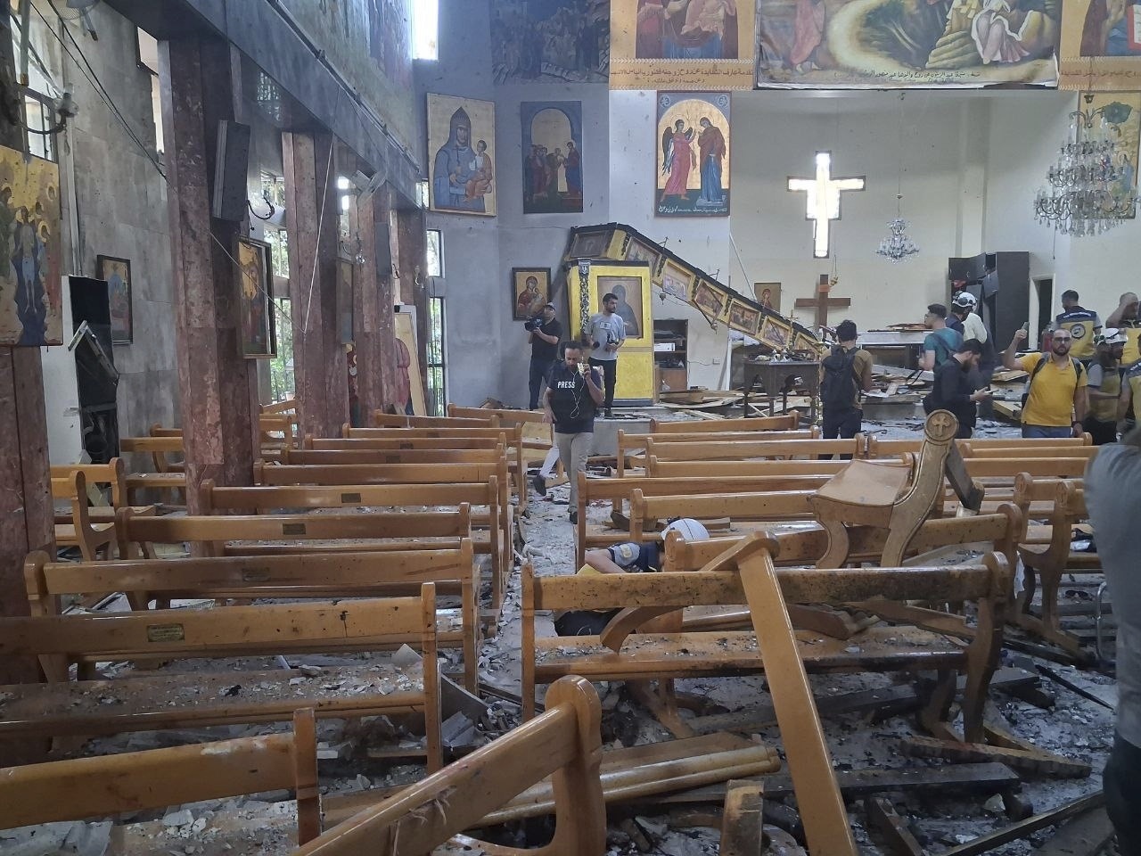 In this photo released by the Syrian official news agency SANA, journalists and Civil Defence workers inspect the damage inside Mar Elias church where a suicide bomber detonated himself in Dweil'a in the outskirts of Damascus, Syria, Sunday June 22, 2025. (SANA via AP)