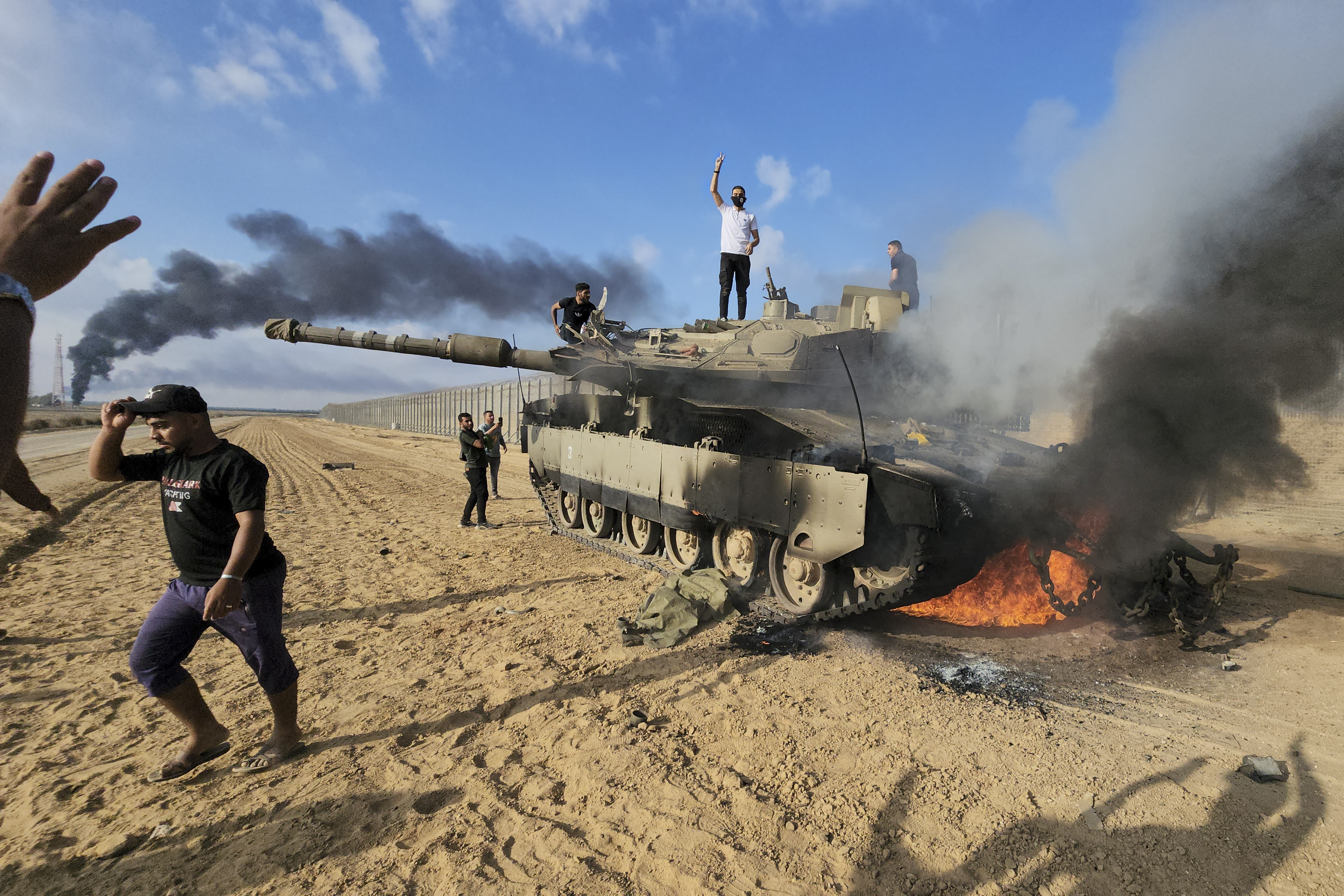 FILE - Palestinians celebrate by a destroyed Israeli tank at the border fence between Israel and the Gaza Strip, east of Khan Younis, during a surprise attack on Israel, Saturday, Oct. 7, 2023. (AP Photo, File)