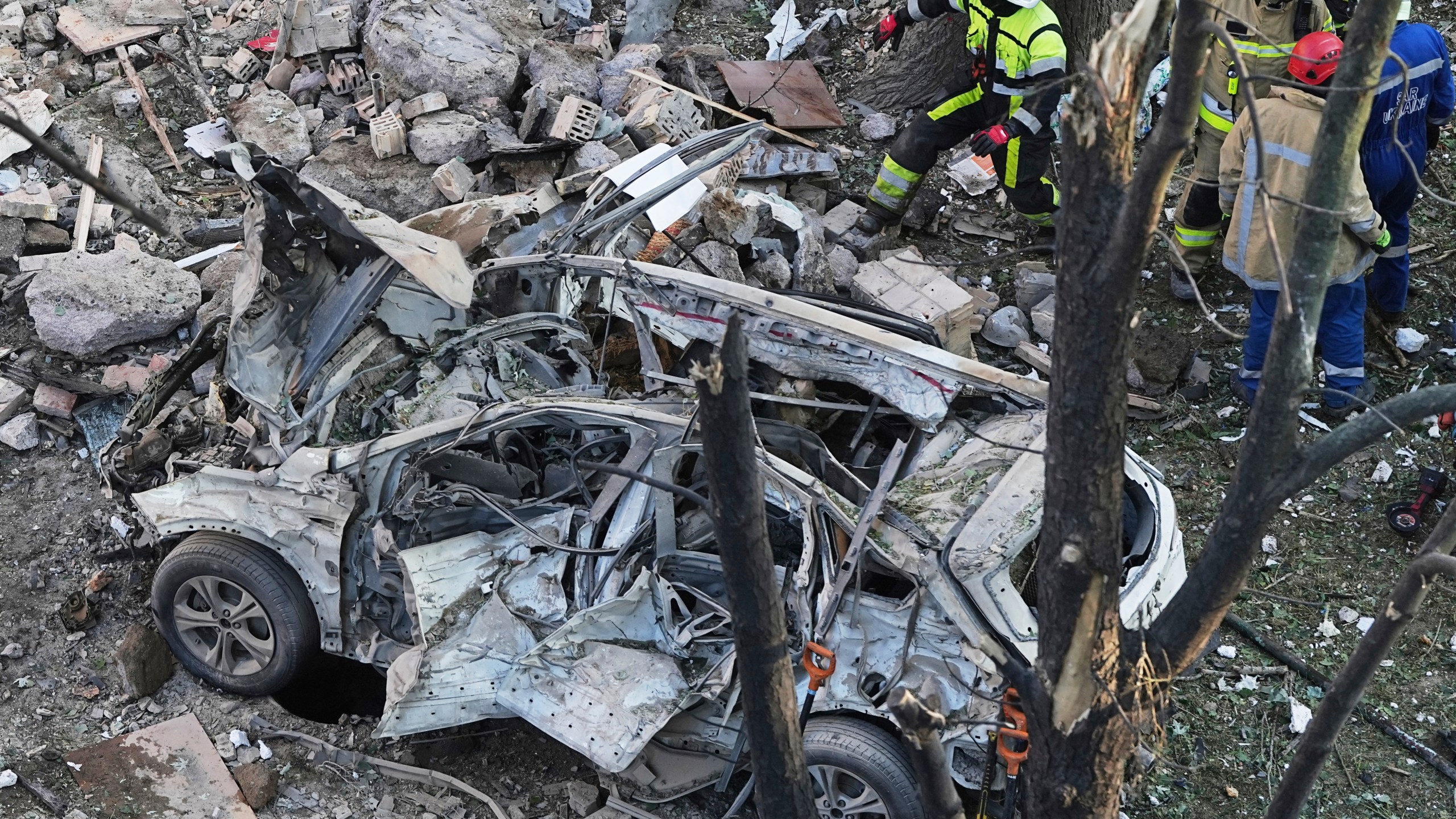 A destroyed car is seen as firefighters work on the site of a damaged building after a Russian attack in Kyiv, Ukraine, early Monday, June 23, 2025. (AP Photo/Efrem Lukatsky)