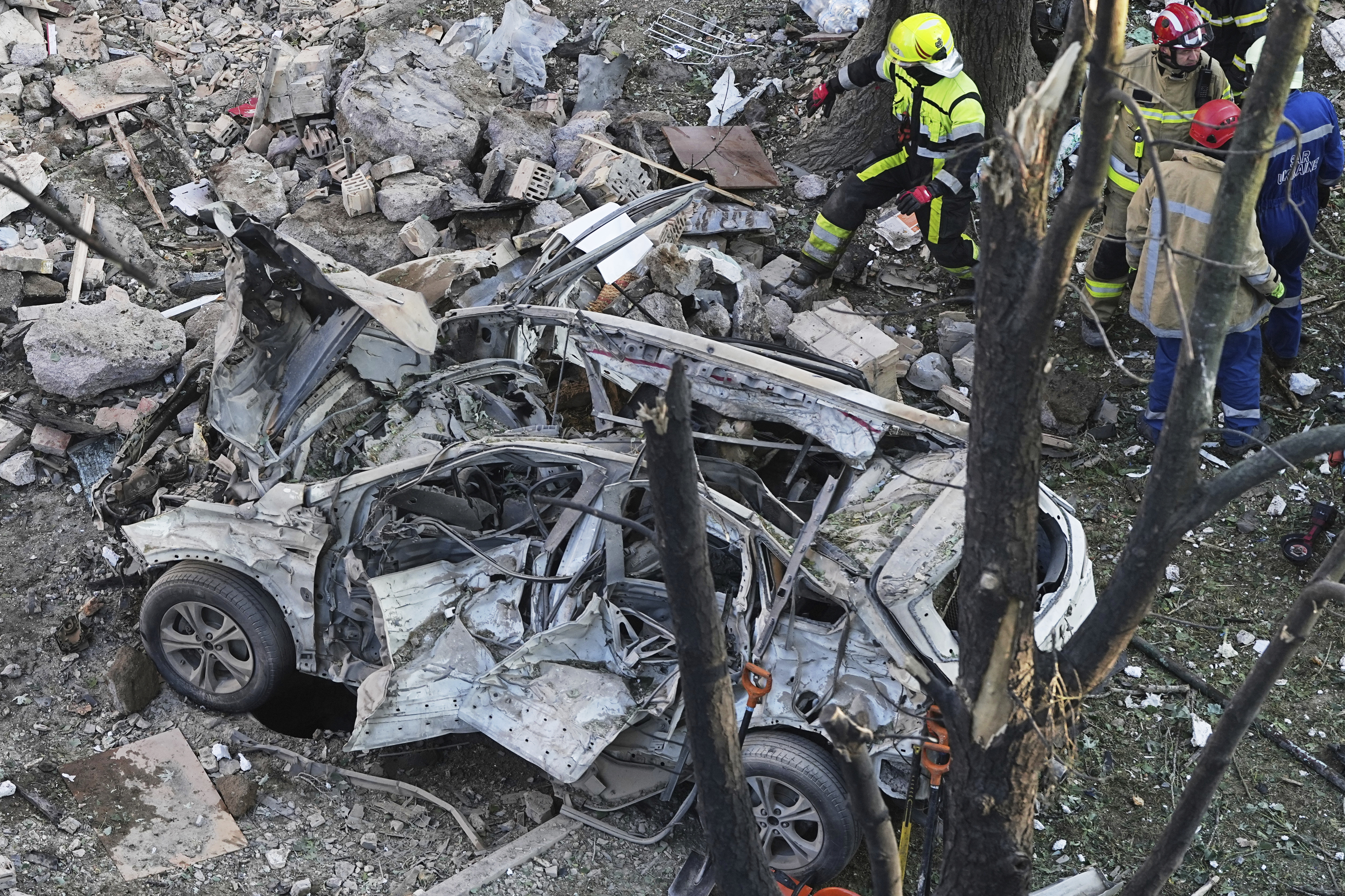 A destroyed car is seen as firefighters work on the site of a damaged building after a Russian attack in Kyiv, Ukraine, early Monday, June 23, 2025. (AP Photo/Efrem Lukatsky)