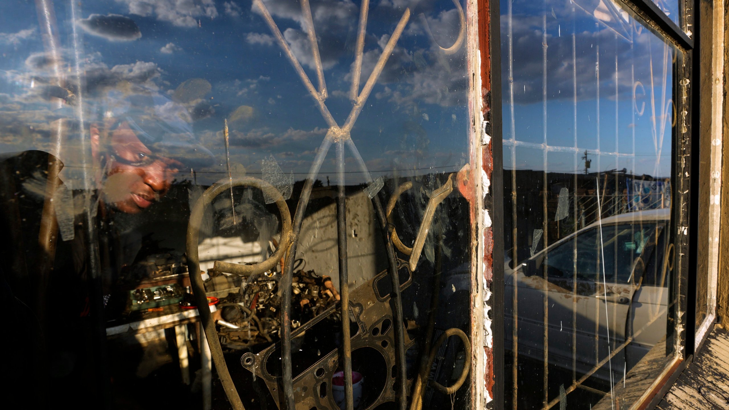 Themba Maseko, a 39-year-old mechanic, peeks through a window inside a workshop in Brakpan, east of Johannesburg, South Africa, Wednesday, April 30, 2025. (AP Photo/Themba Hadebe)