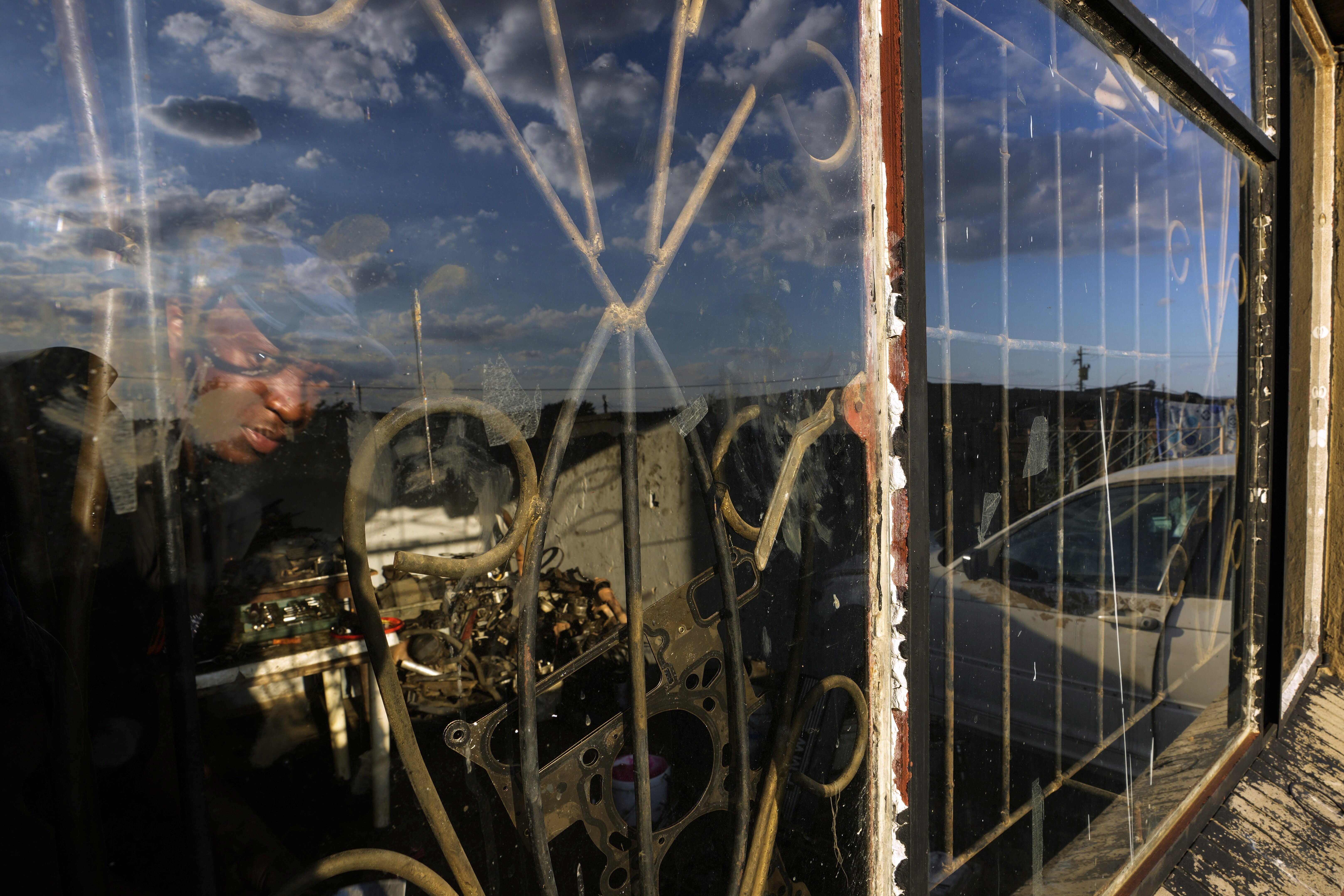 Themba Maseko, a 39-year-old mechanic, peeks through a window inside a workshop in Brakpan, east of Johannesburg, South Africa, Wednesday, April 30, 2025. (AP Photo/Themba Hadebe)