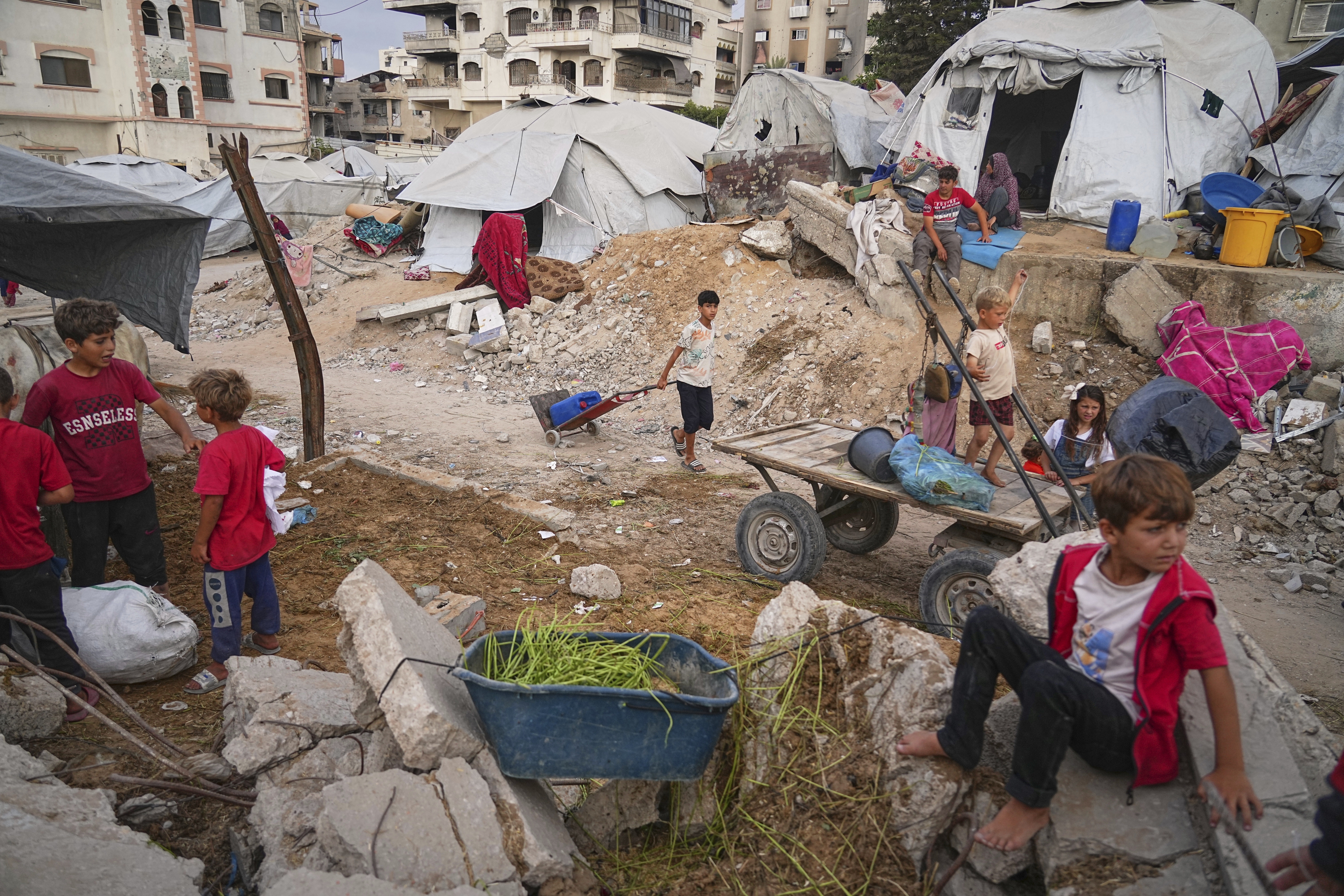 Palestinian youth and children are seen at a tent camp set up amid war-damaged infrastructure in Gaza City, Monday, June 23, 2025. (AP Photo/Jehad Alshrafi)