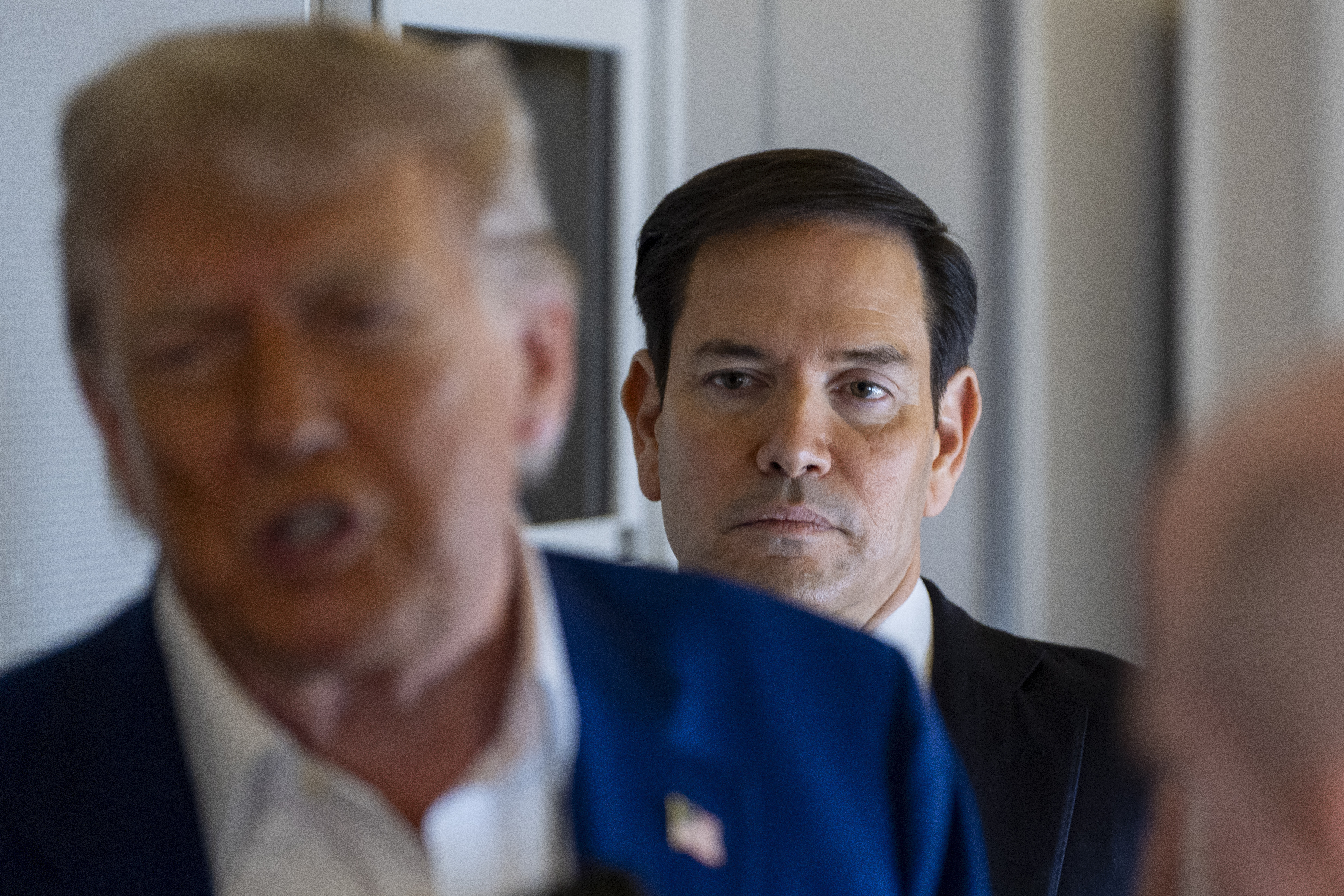 Secretary of State Marco Rubio stands behind as President Donald Trump speaks with reporters on Air Force One while in flight from Joint Base Andrews, Md., to Amsterdam, Netherlands, Tuesday, June 24, 2025. (AP Photo/Alex Brandon)