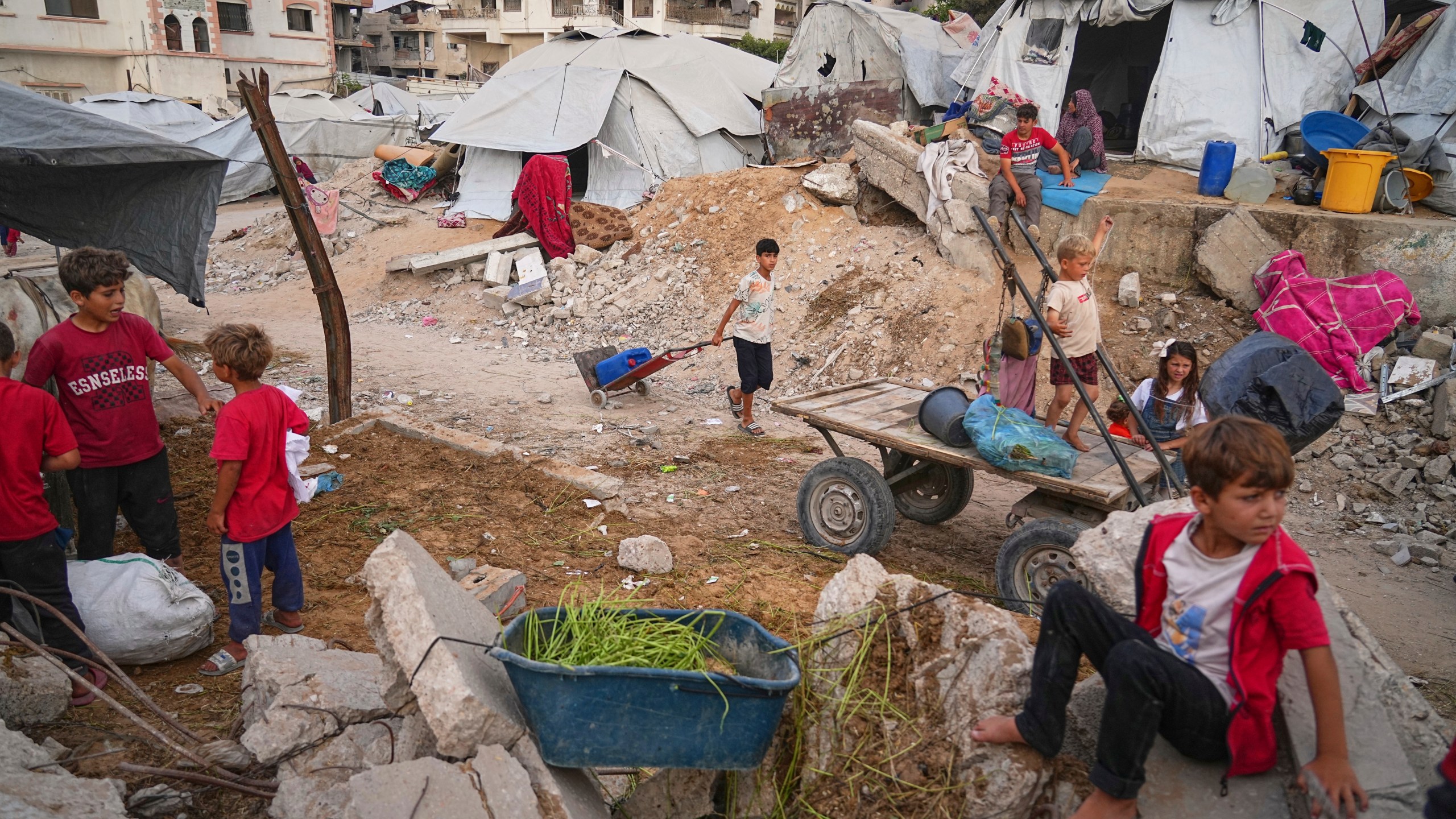 Palestinian youth and children are seen at a tent camp set up amid war-damaged infrastructure in Gaza City, Monday, June 23, 2025. (AP Photo/Jehad Alshrafi)