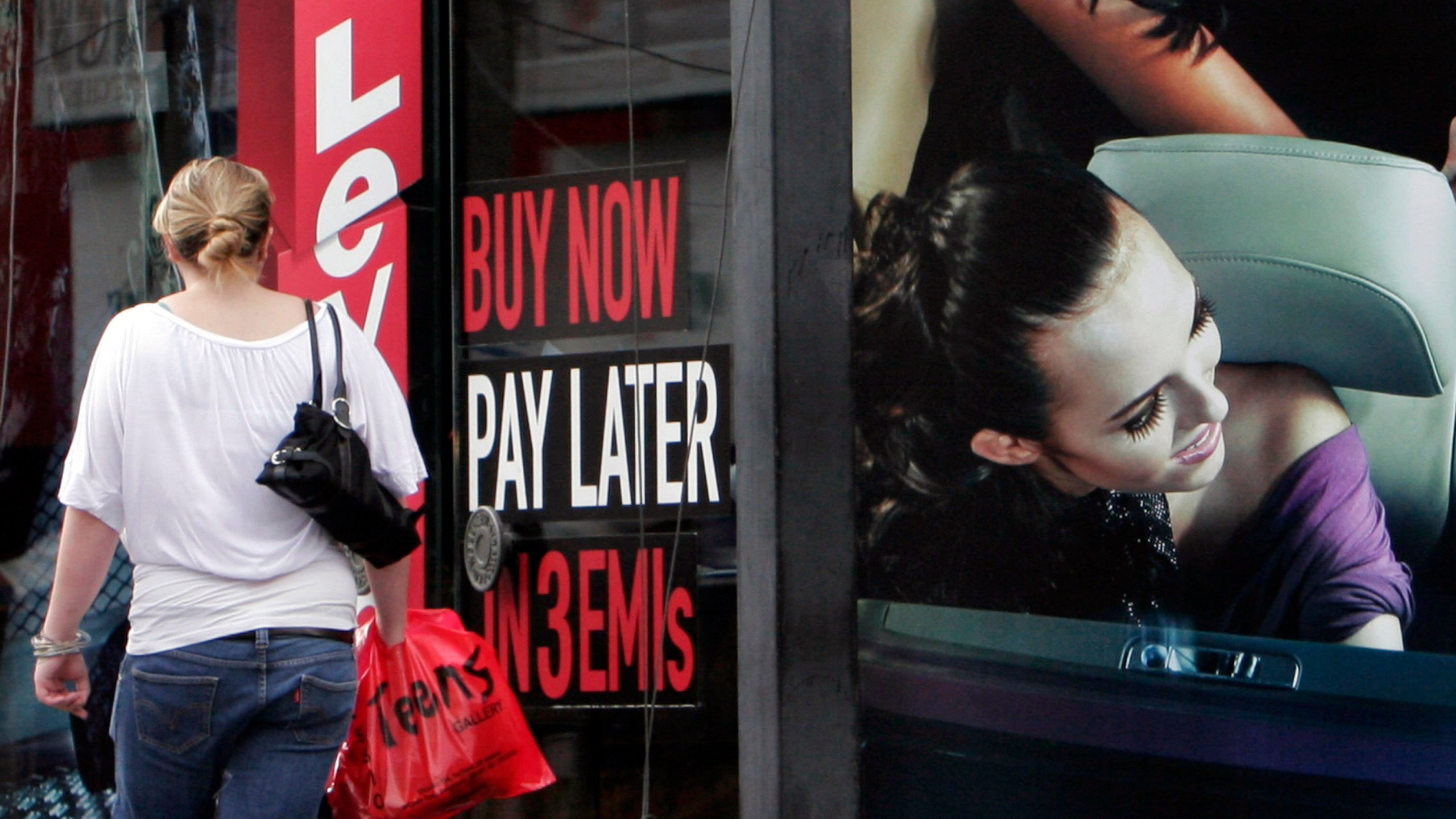 FILE - A woman walks by a sign "Buy now pay later" at a store in Bangalore, India, on Sept. 10, 2009. (AP Photo/Aijaz Rahi, File)