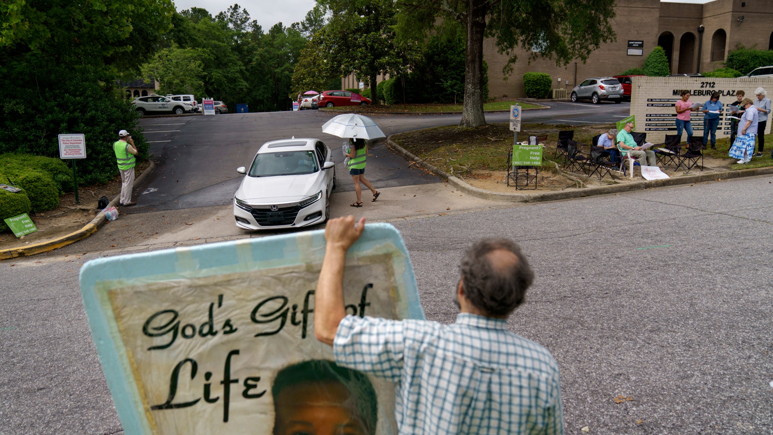 FILE - Anti-abortion protester Steven Lefemine holds a sign as the anti-abortion group, A Moment of Hope, wearing green vests, tries to talk with patients arriving for abortion appointments at Planned Parenthood as a group of Catholics pray off to the side, May 27, 2022, in Columbia, S.C. (AP Photo/David Goldman, File)