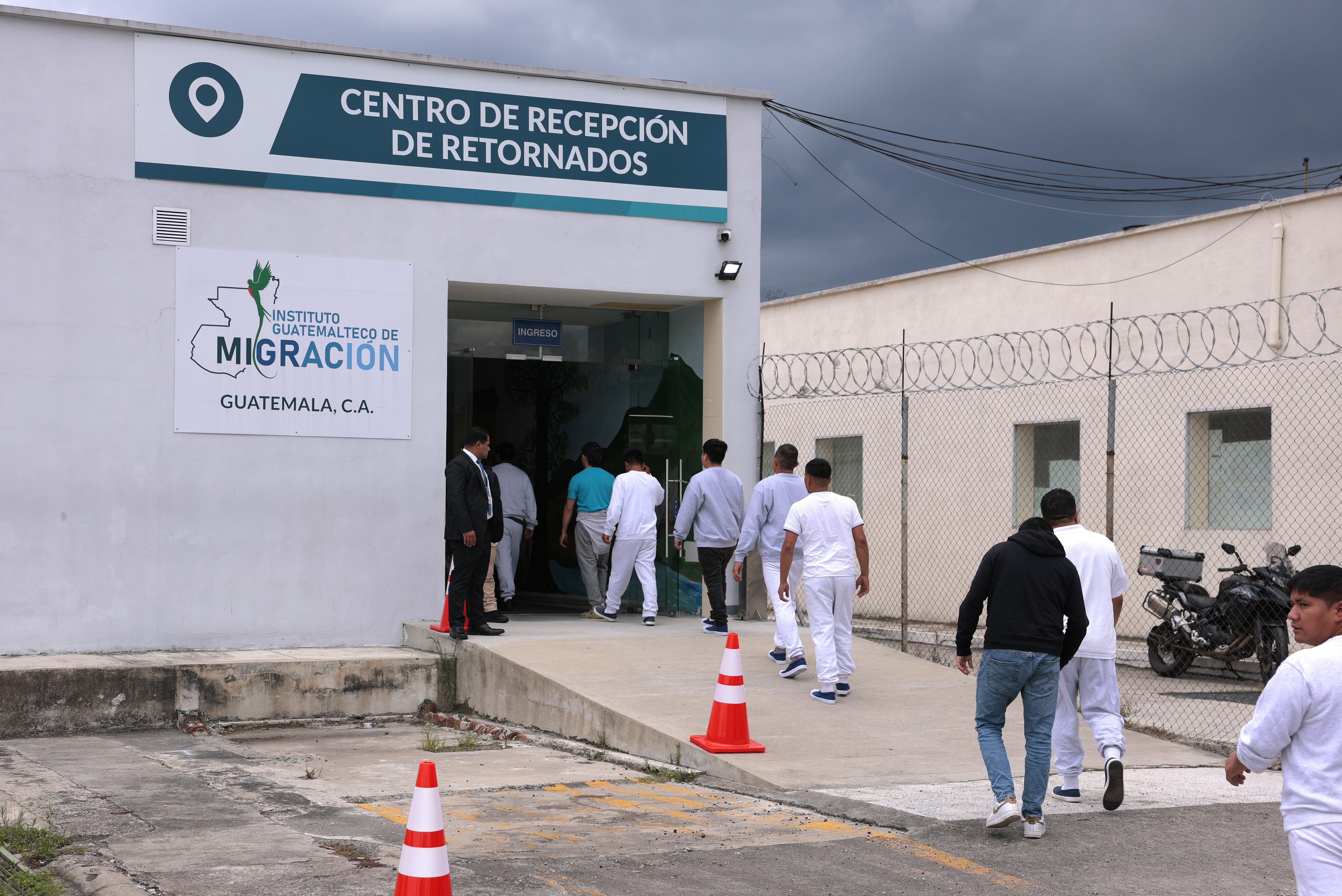People deported from the United States walk into a processing center after arriving on a repatriation flight, during a Department of Homeland Security operations tour for visiting Homeland Security Secretary Kristi Noem, at La Aurora International Airport in Guatemala City, Thursday, June 26, 2025. (Anna Moneymaker/Pool Photo via AP)