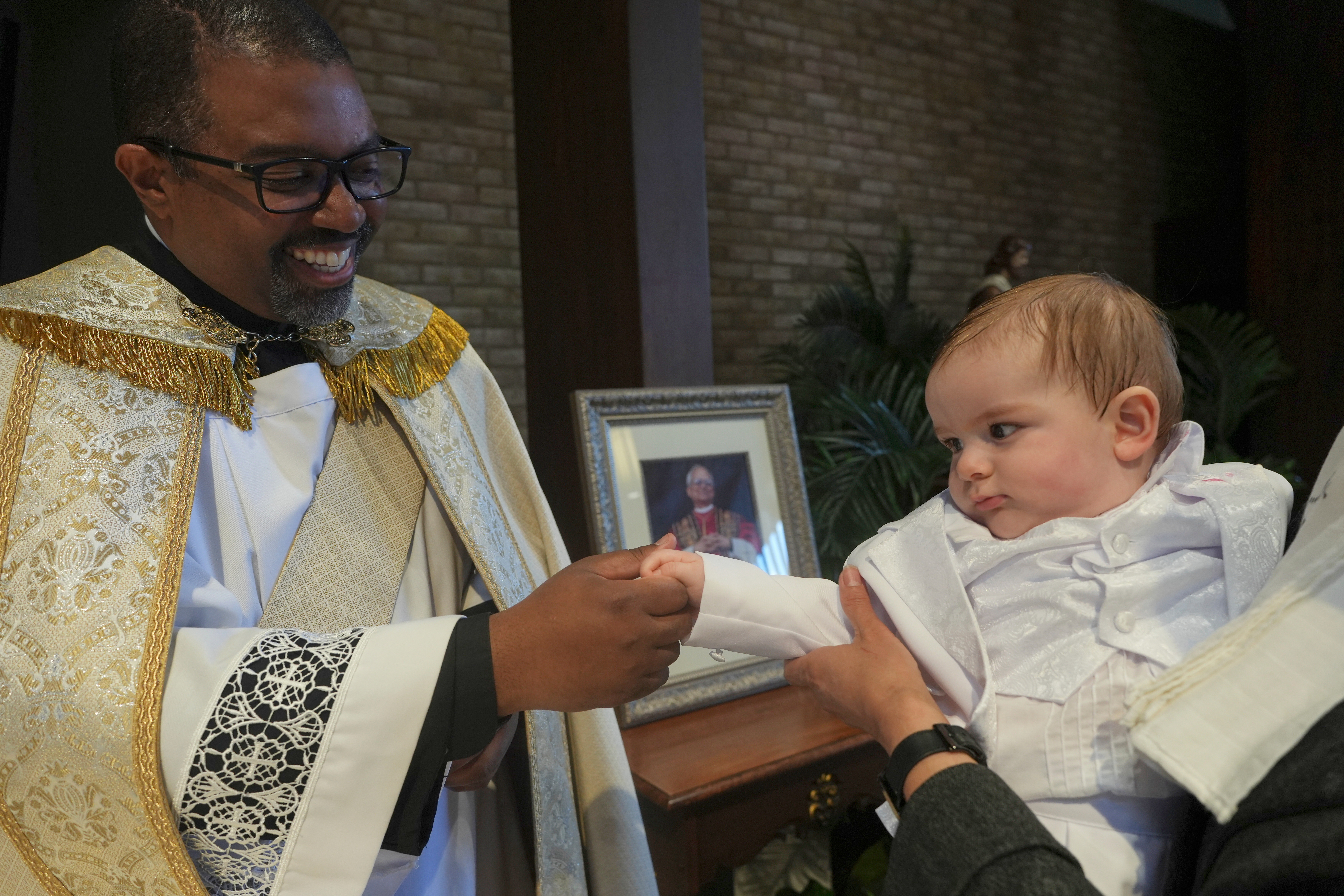 The Rev. Ricky Malebranche holds the hand of 9-month-old Andres Roman Marquez after baptizing him at St. Louis Catholic Church in Alexandria, Va., on Saturday, May 24, 2025. (AP Photo/Luis Andres Henao)