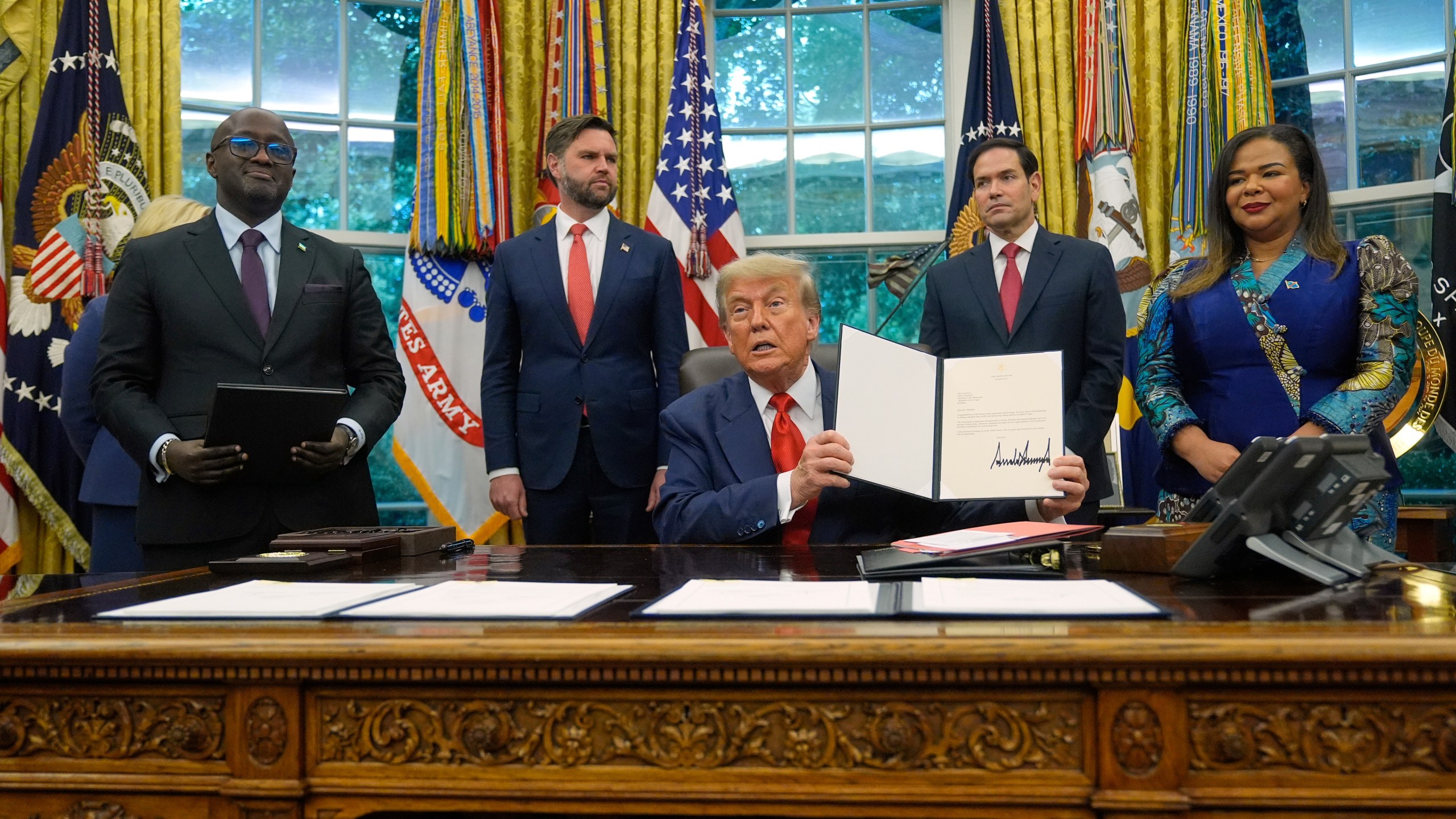 President Donald Trump holds up a signed document to present to Congo's Foreign Minister Therese Kayikwamba Wagner, right, as Rwanda's Foreign Minister Olivier Nduhungirehe, from left, Vice President JD Vance and Secretary of State Marco Rubio watch, Friday, June 27, 2025, in the Oval Office at the White House in Washington. (AP Photo/Manuel Balce Ceneta)