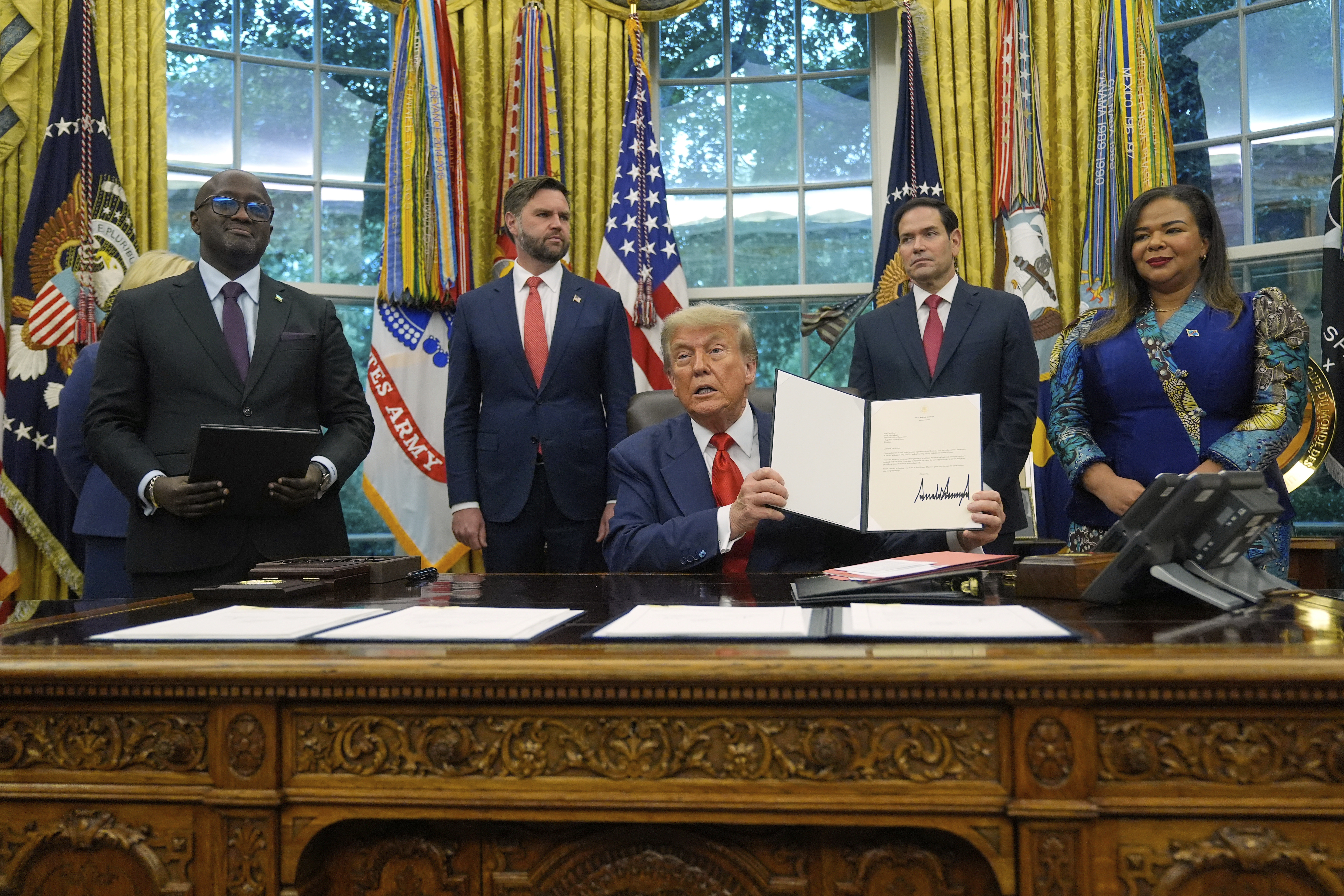 President Donald Trump holds up a signed document to present to Congo's Foreign Minister Therese Kayikwamba Wagner, right, as Rwanda's Foreign Minister Olivier Nduhungirehe, from left, Vice President JD Vance and Secretary of State Marco Rubio watch, Friday, June 27, 2025, in the Oval Office at the White House in Washington. (AP Photo/Manuel Balce Ceneta)
