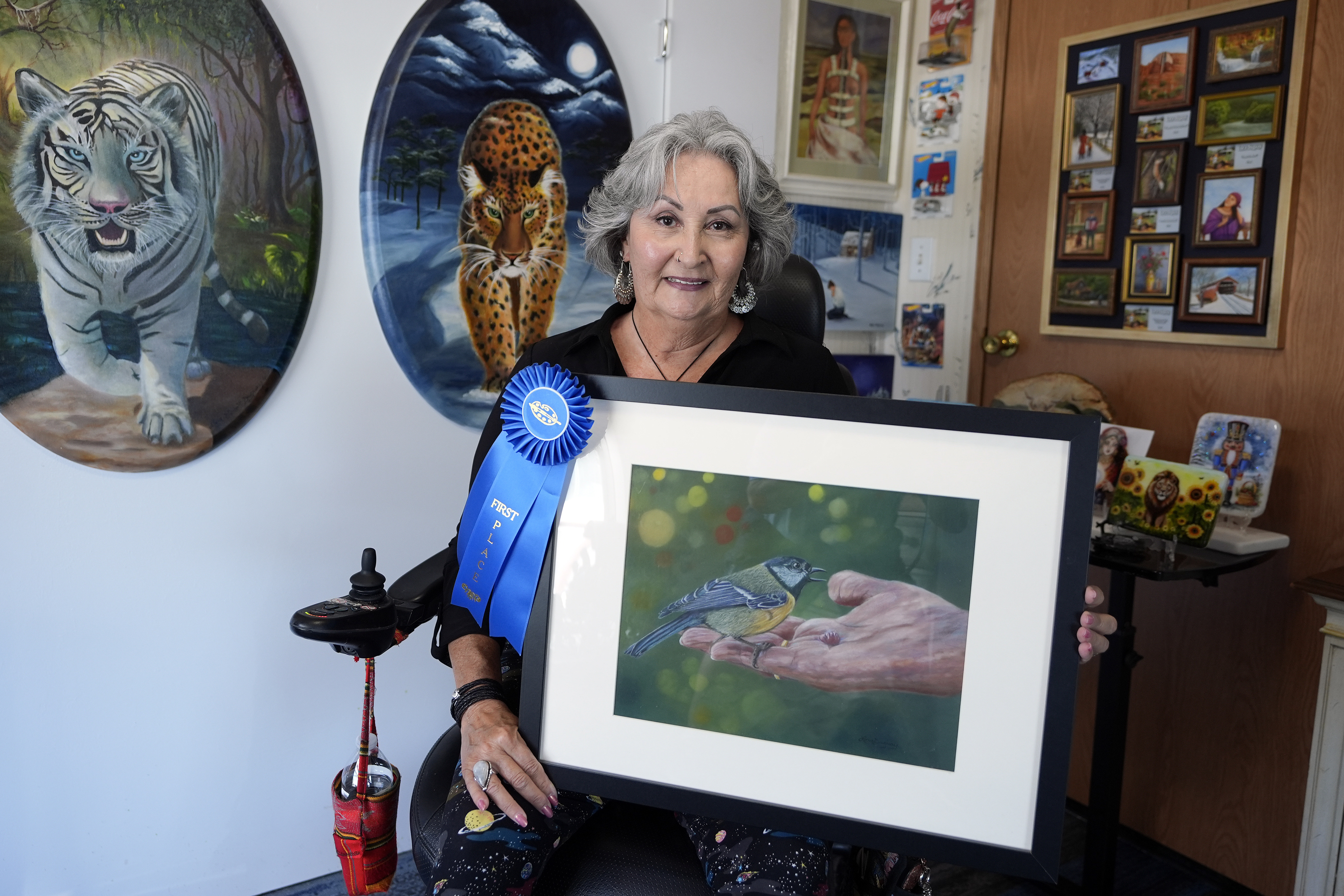 Artist Lora Duguay poses for a portrait in her wheelchair with some of her artwork at home in Clearwater, Fla., on Tuesday, June 10, 2025. (AP Photo/Chris O'Meara)