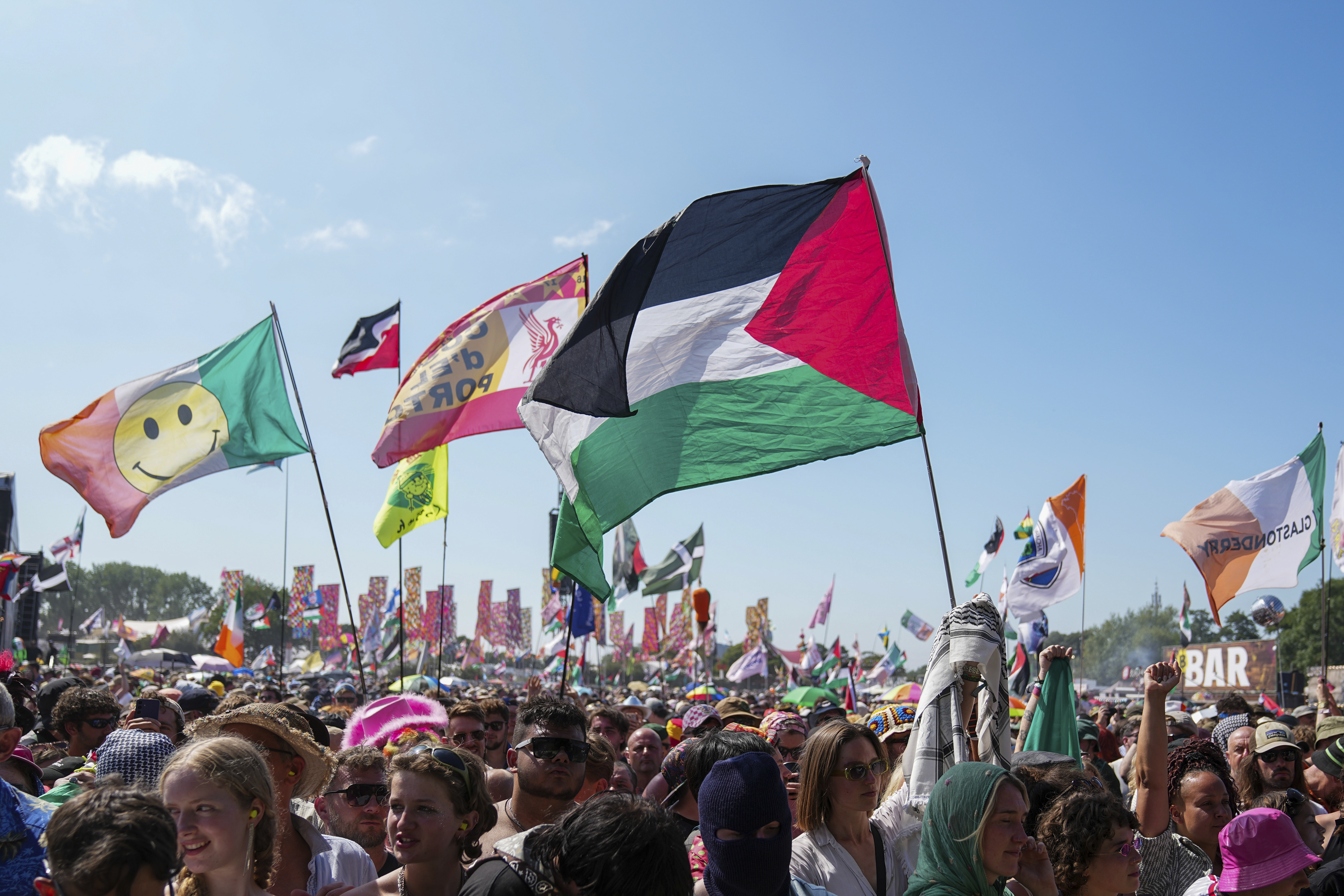 The flag of Palestine is waved in a crowd of festivalgoers at the hip hop trio Kneecap's performance during the Glastonbury Festival in Worthy Farm, Somerset, England, Saturday, June 28, 2025. (Scott A Garfitt/Invision/AP)