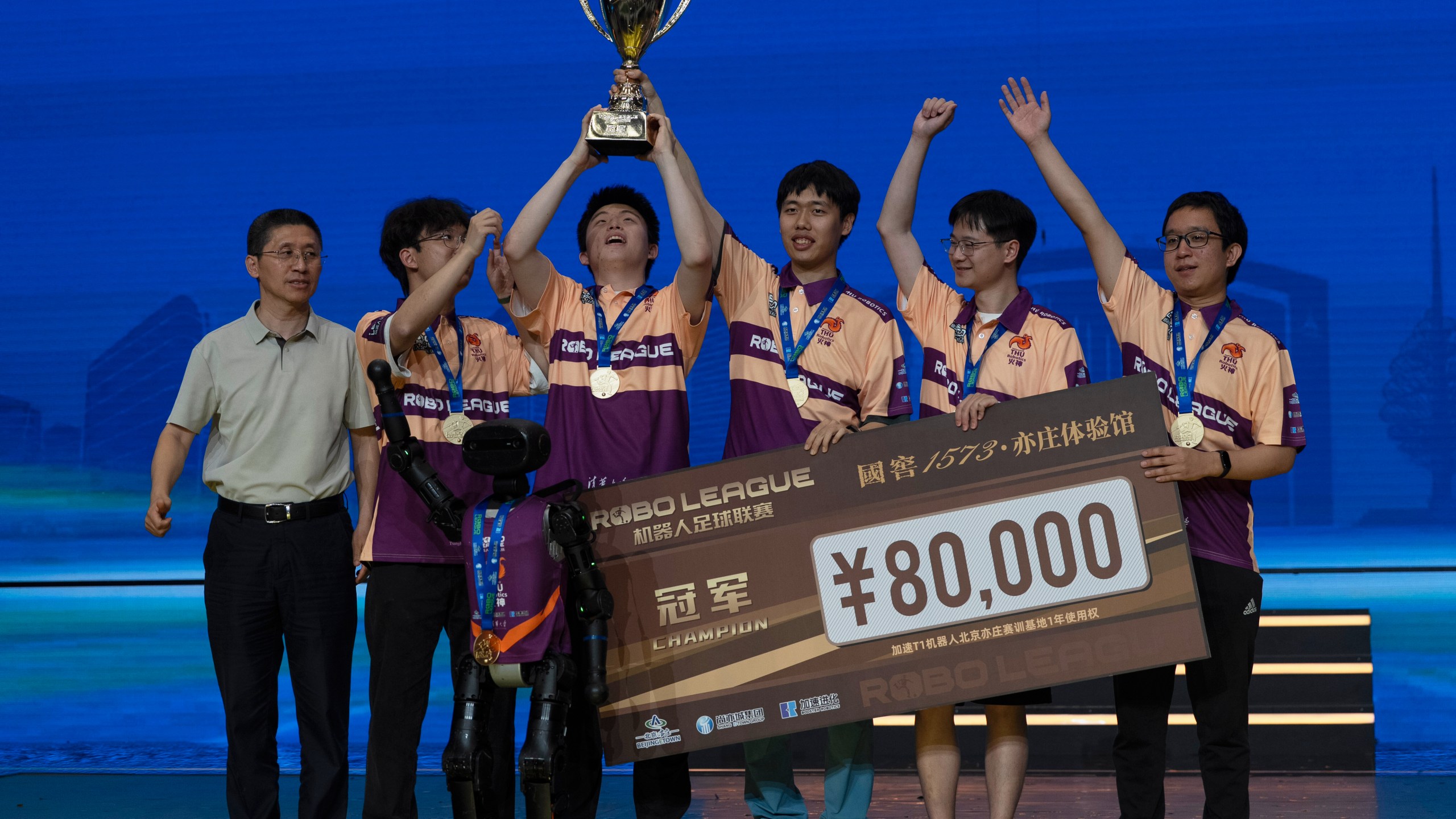 The human members of Team THU celebrate with their trophy near a T1 robot from Booster Robotics used during the inaugural RoBoLeague robot soccer competition held in Beijing, Saturday, June 28, 2025. (AP Photo/Ng Han Guan)