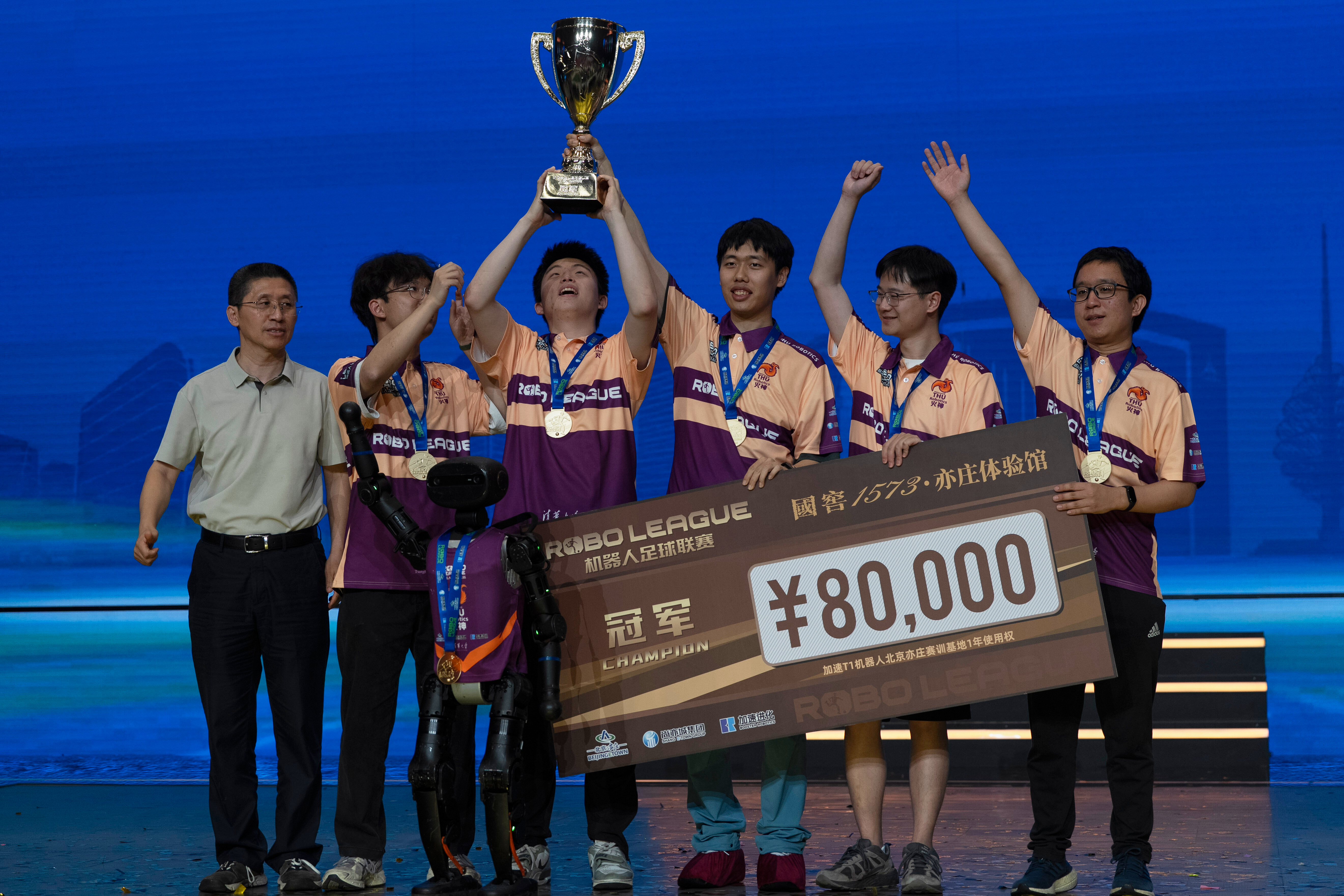 The human members of Team THU celebrate with their trophy near a T1 robot from Booster Robotics used during the inaugural RoBoLeague robot soccer competition held in Beijing, Saturday, June 28, 2025. (AP Photo/Ng Han Guan)