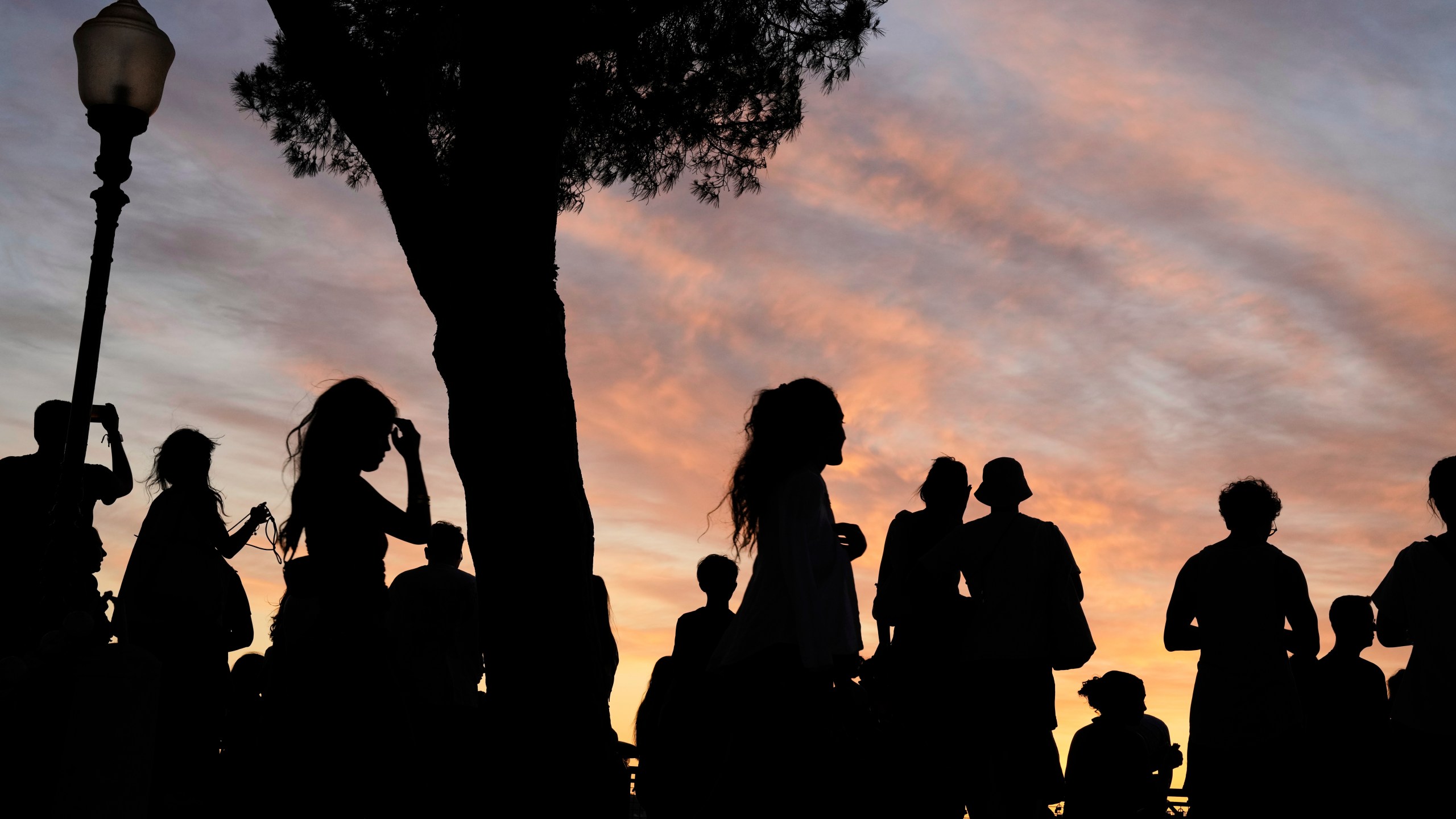 People watch the sun set from the Our Lady of the Hill viewpoint overlooking Lisbon at the end of a hot day in Lisbon, Friday, June 27, 2025. (AP Photo/Armando Franca)