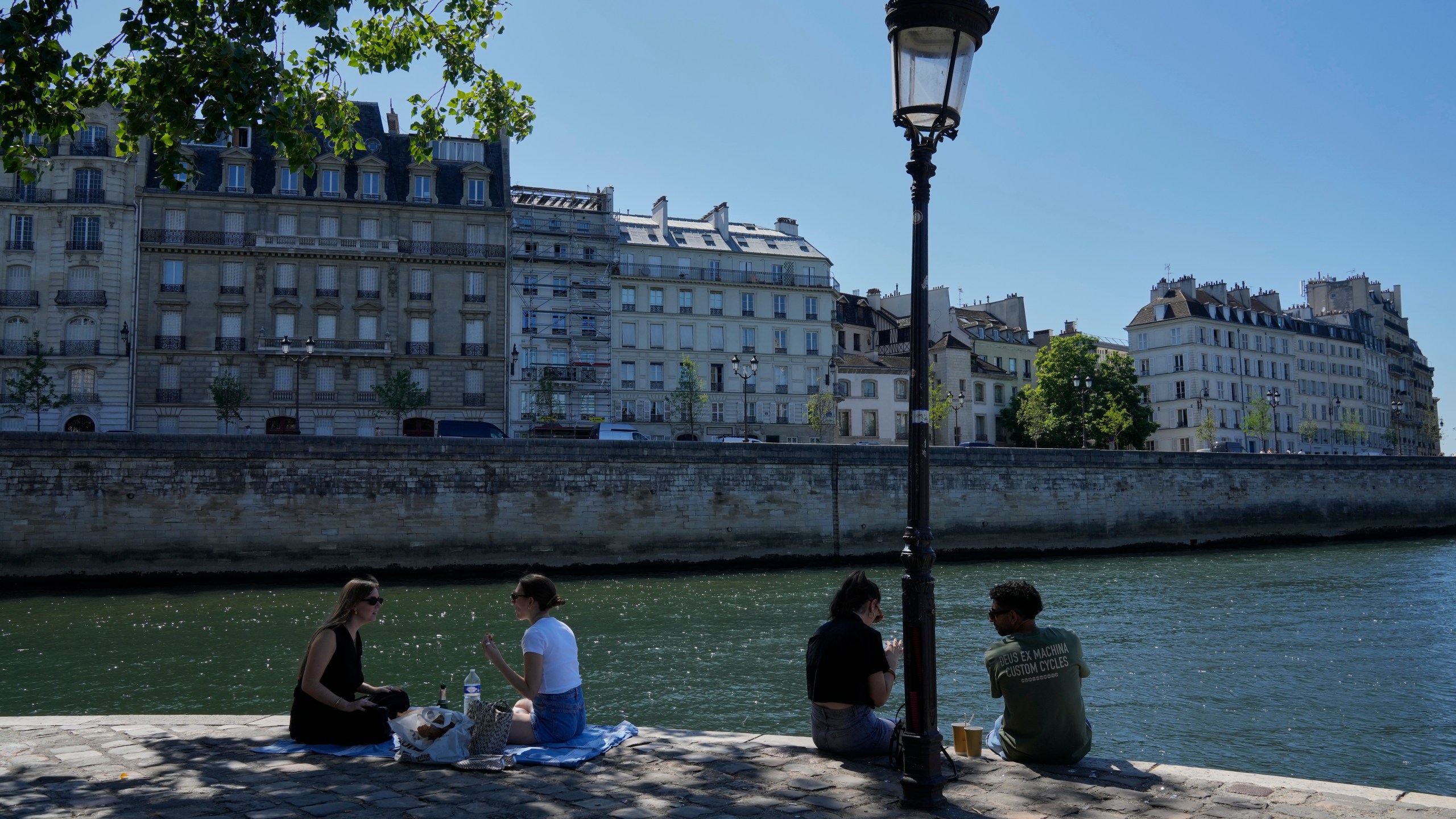 People sit in the shade along the Seine river in Paris, Sunday, June 29, 2025. (AP Photo/Michel Euler)