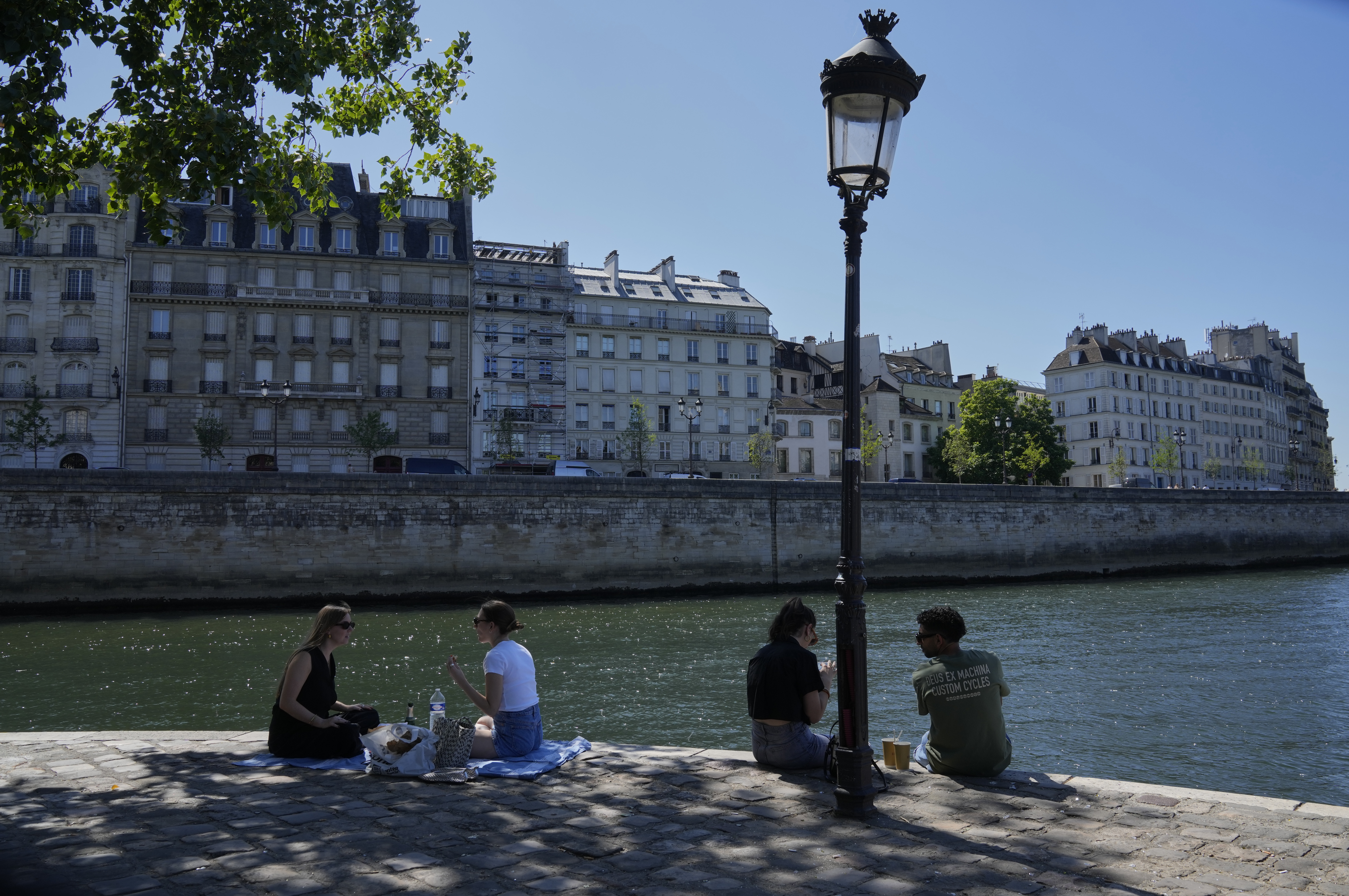 People sit in the shade along the Seine river in Paris, Sunday, June 29, 2025. (AP Photo/Michel Euler)