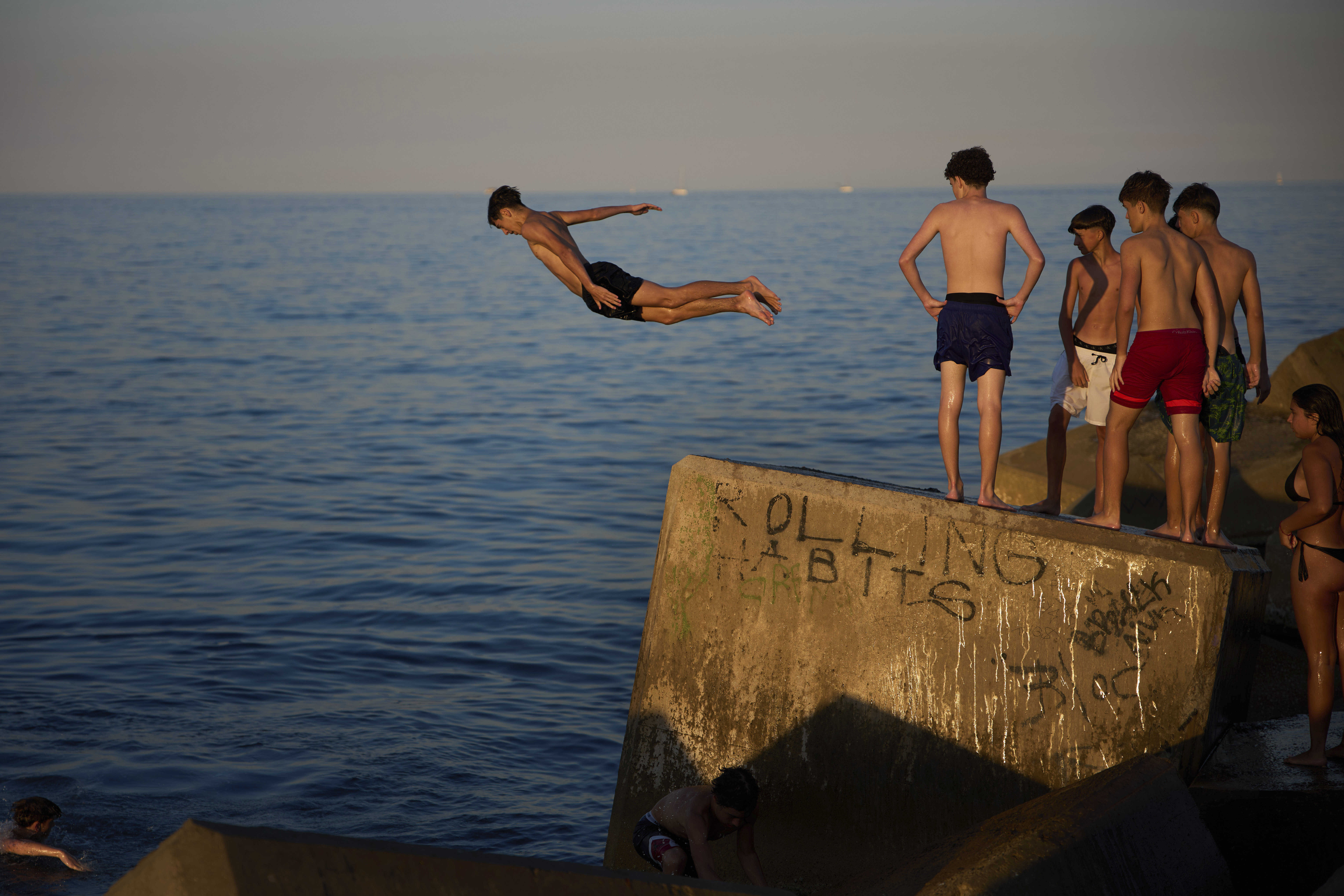 Young swimmers jump into the water from a rock on a breakwater on a hot day in Barcelona, Spain, Sunday, June 29, 2025. (AP Photo/Emilio Morenatti)