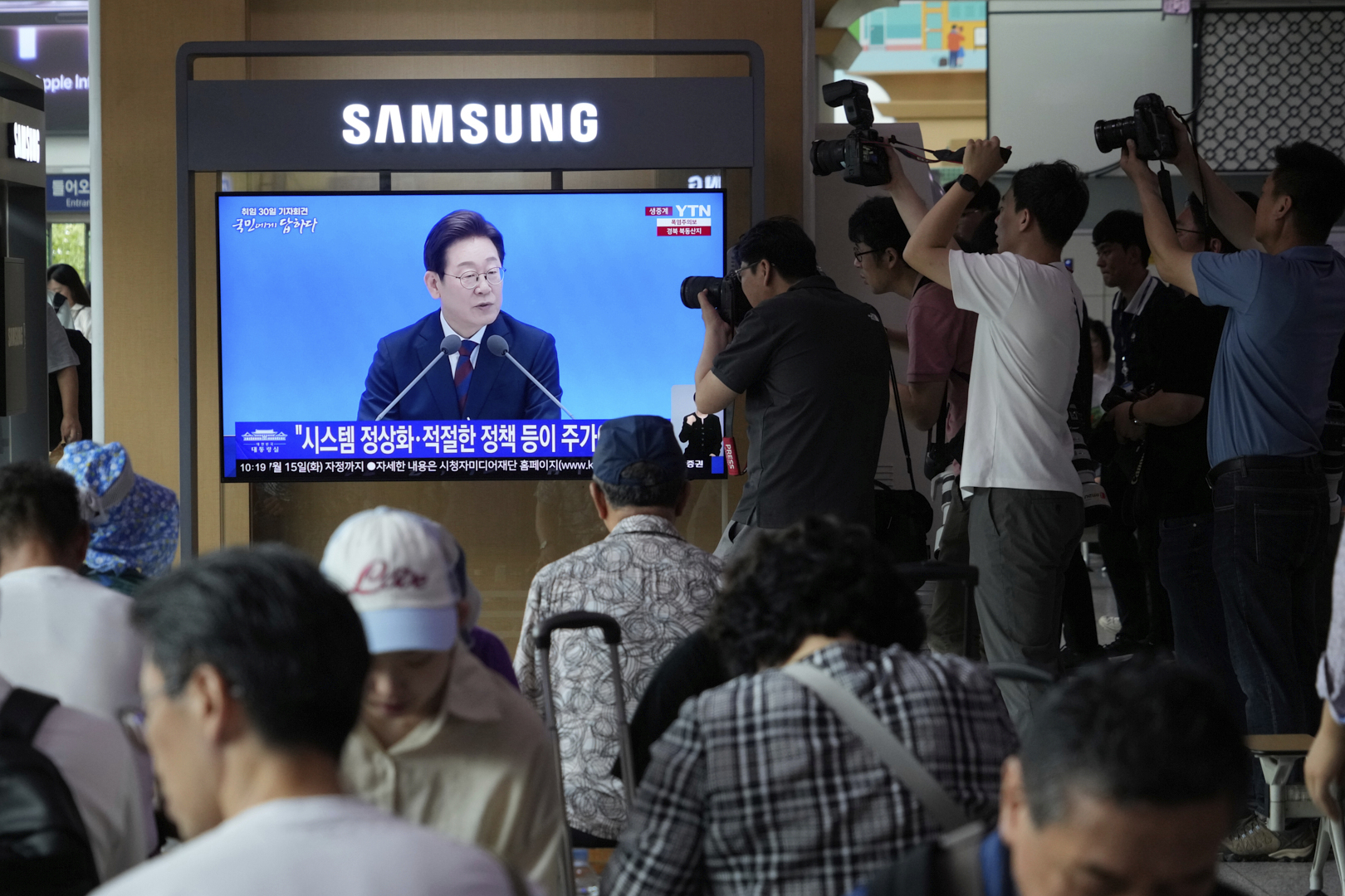 People watch a TV screen showing the live broadcast of South Korean President Lee Jae Myung's press conference at the Seoul Railway Station in Seoul, South Korea, Thursday, July 3, 2025. (AP Photo/Ahn Young-joon)