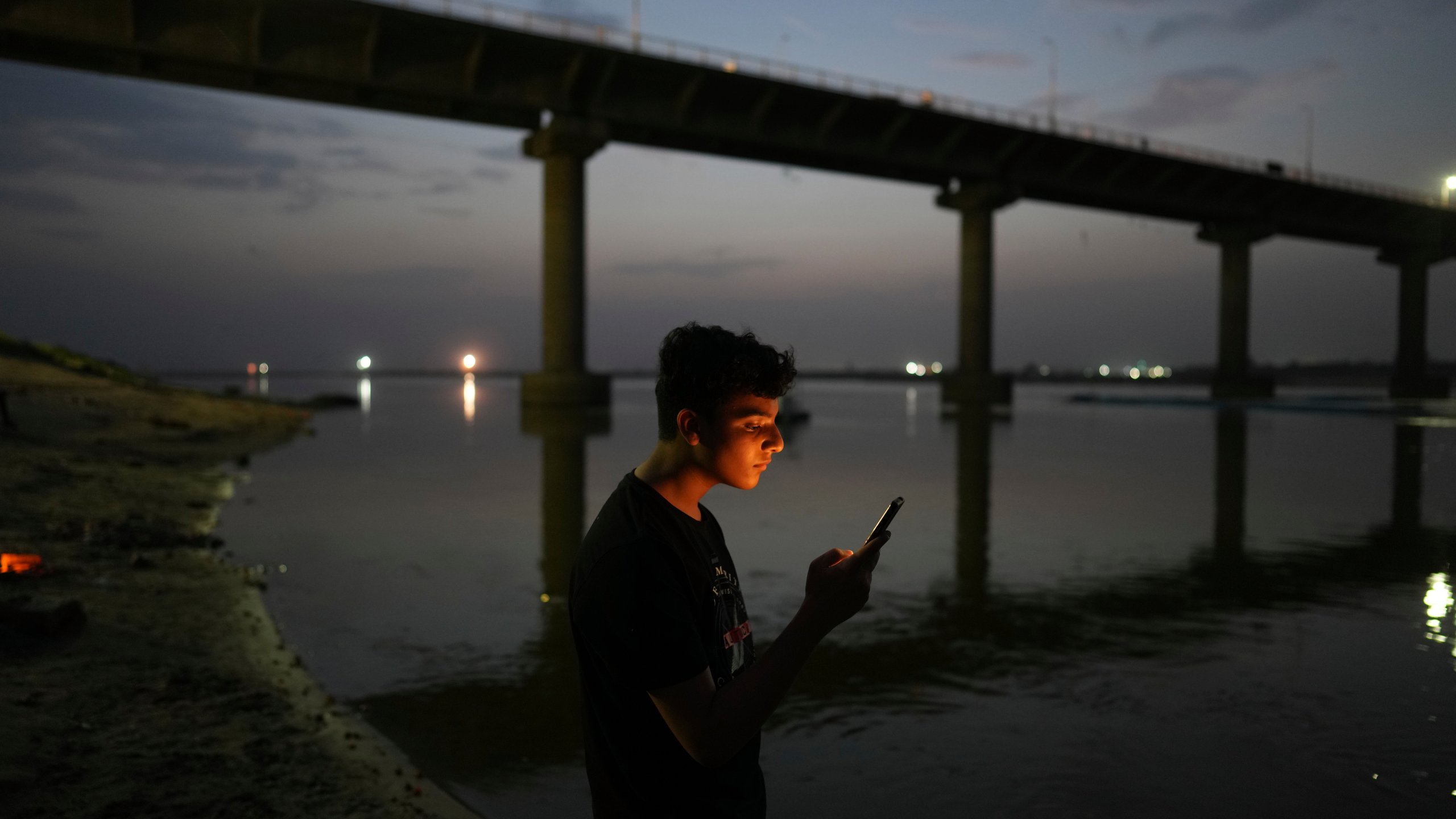 FILE - A youth checks his mobile phone on the bank of the River Ganges in Prayagraj, India, June 7, 2023. (AP Photo/Rajesh Kumar Singh, File)