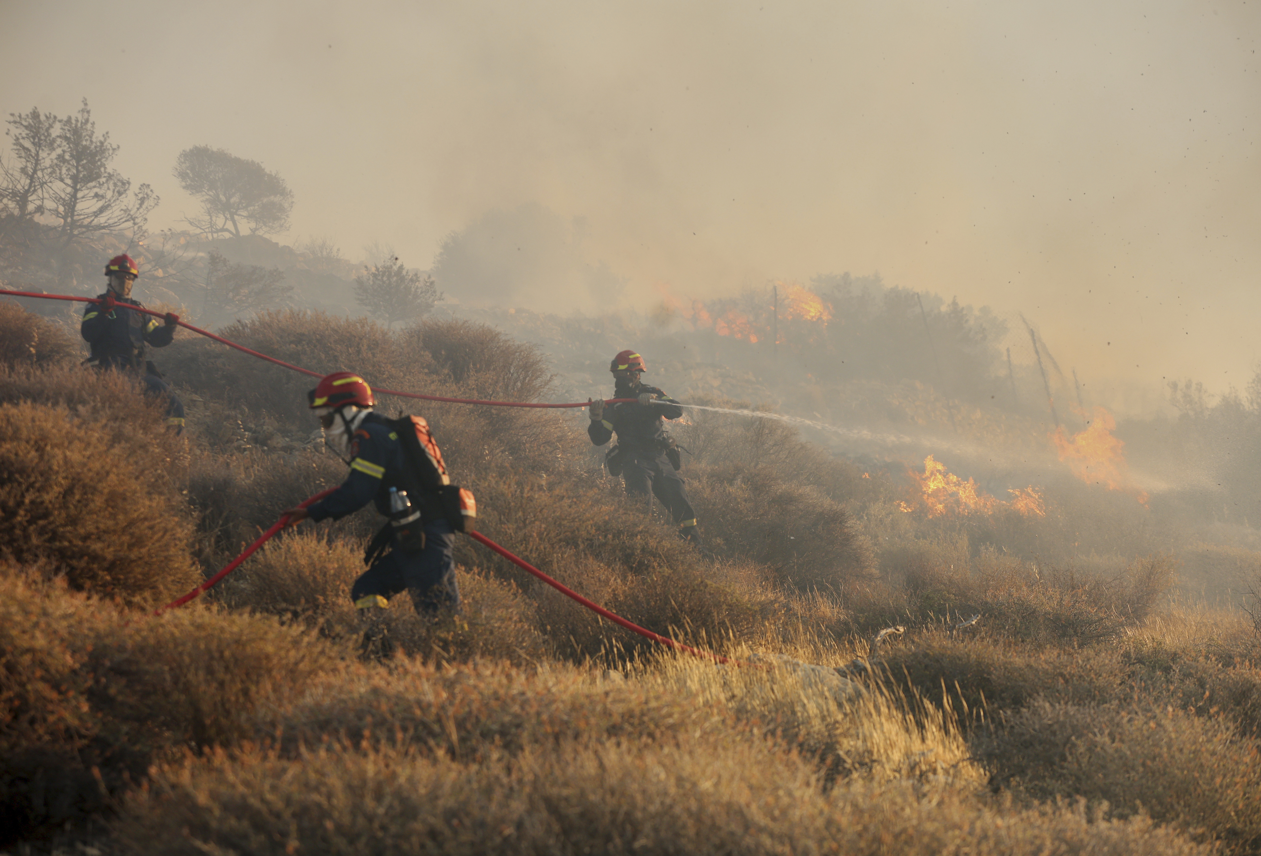 Firefighter uses a hose as the try to extinguish the blaze near the town of Ierapetra on the south coast of Crete island, Greece, Thursday July 3, 2025, as a fast-moving wildfire prompted authorities to clear villages and coastal areas, officials said. (InTime News via AP)