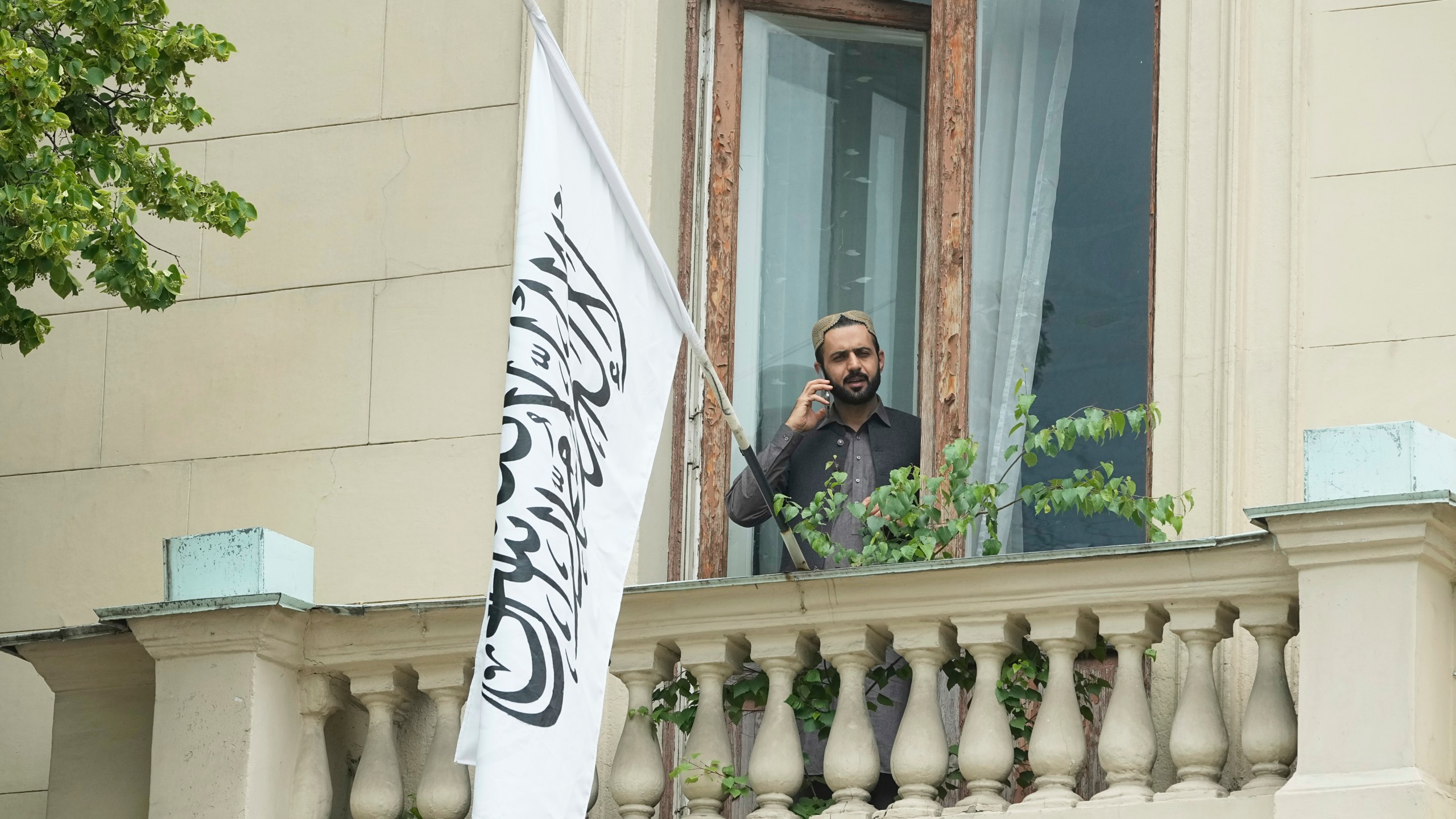 A man talks by a phone while standing on a balcony of the Afghan Embassy in Moscow, Russia, Friday, July 4, 2025, where the flag of the Islamic Emirate of Afghanistan was raised after Russia recognized the Taliban government in Afghanistan. (AP Photo/Pavel Bednyakov)