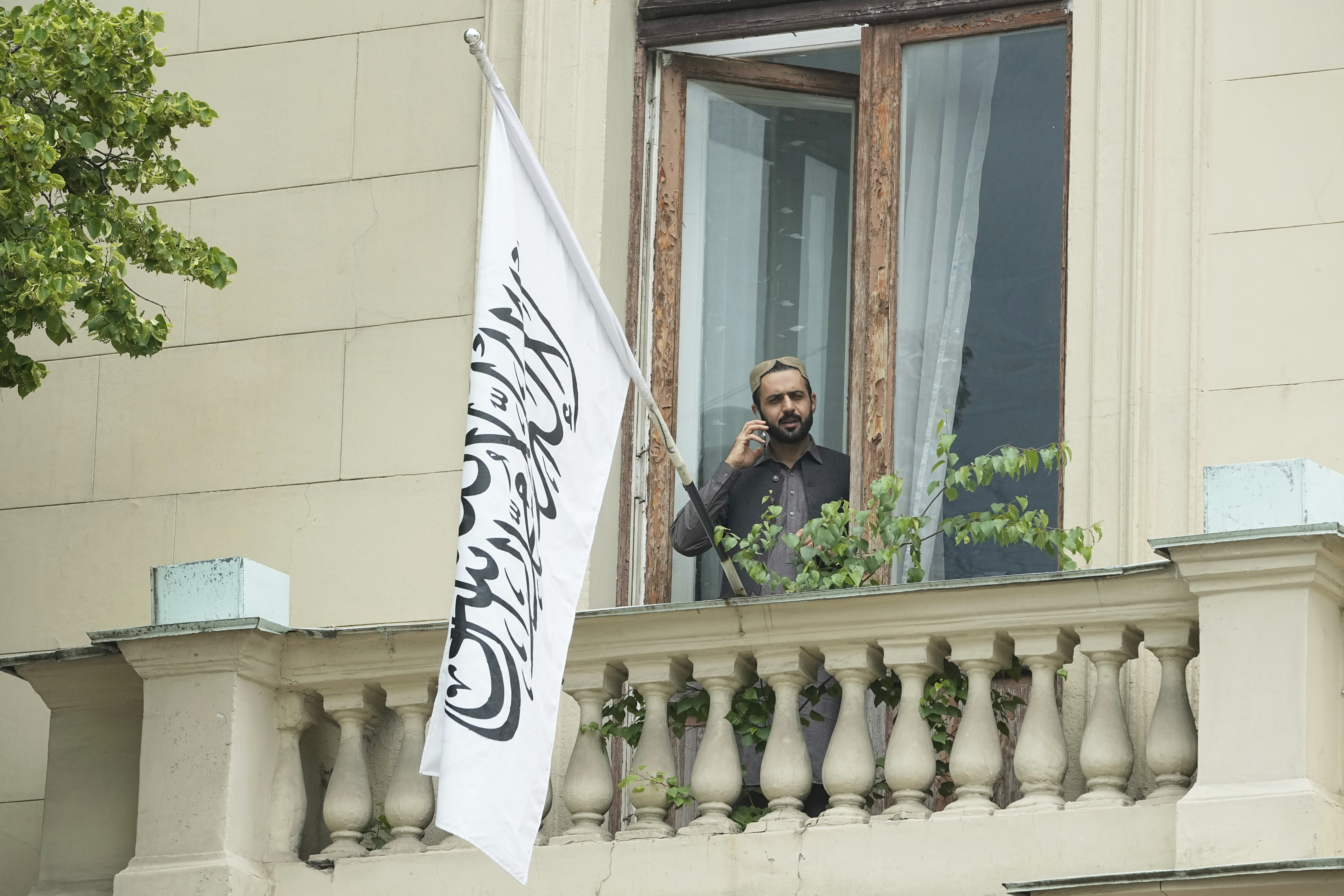 A man talks by a phone while standing on a balcony of the Afghan Embassy in Moscow, Russia, Friday, July 4, 2025, where the flag of the Islamic Emirate of Afghanistan was raised after Russia recognized the Taliban government in Afghanistan. (AP Photo/Pavel Bednyakov)