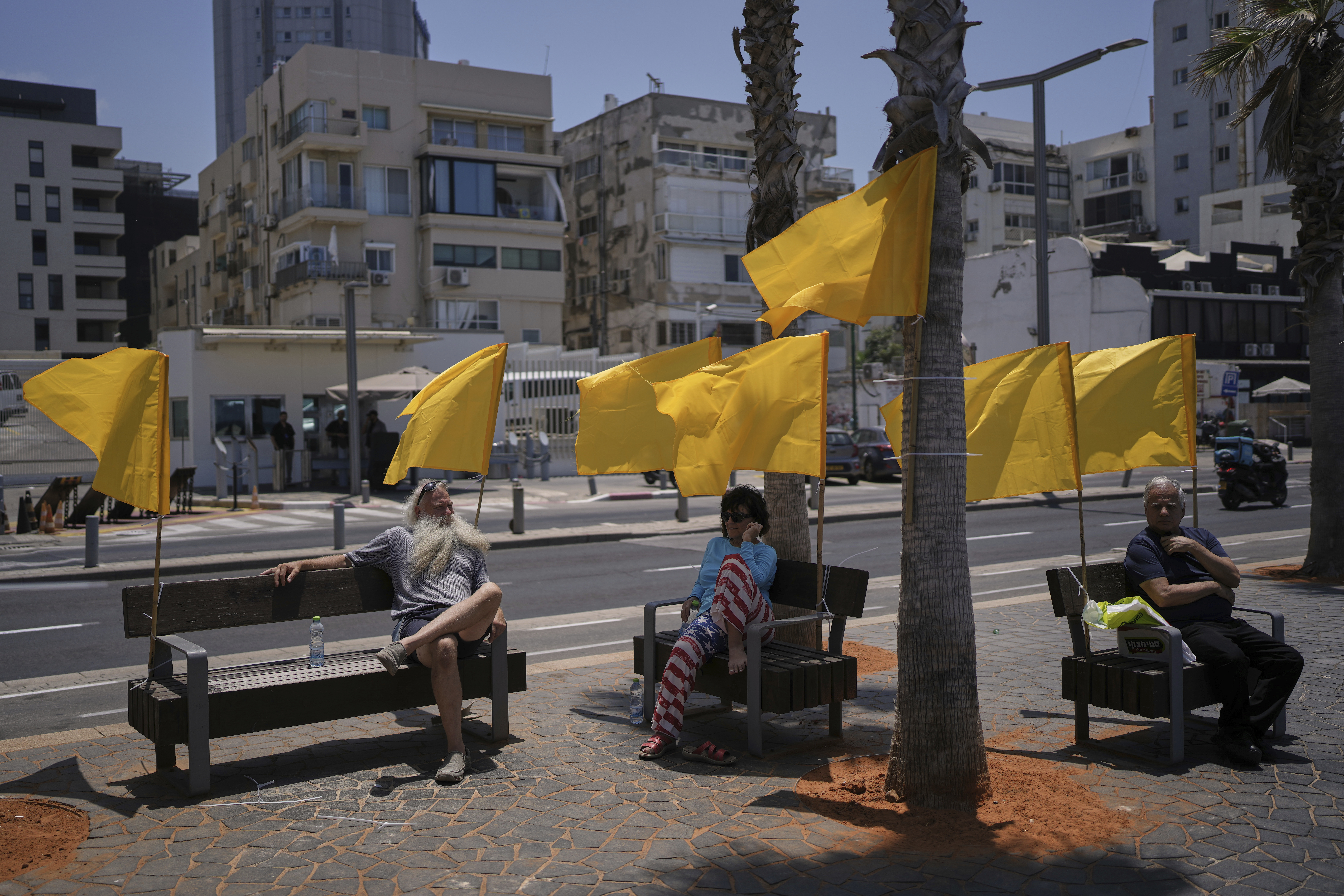 People sit on benches, decorated with yellow flags symbolizing the hostages being held by Hamas in the Gaza Strip, at the beachfront in Tel Aviv, Israel, Friday, July 4, 2025. (AP Photo/Oded Balilty)