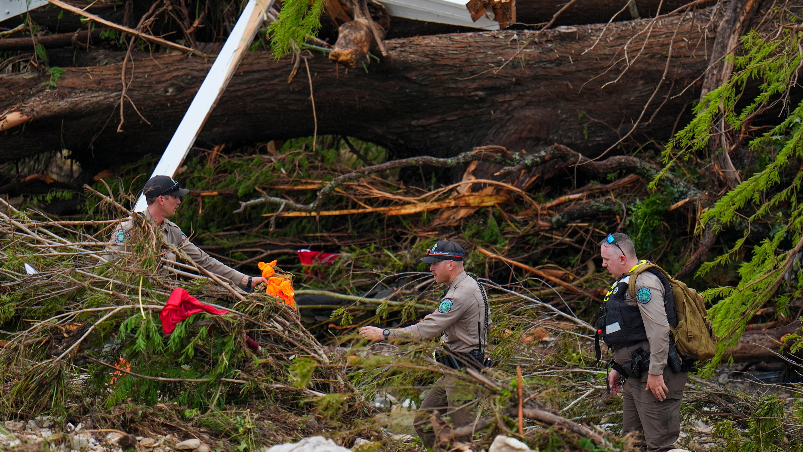 Officials with the Texas Game Warden comb through debris along the banks of the Guadalupe River after a flash flood swept through the area Saturday, July 5, 2025, in Hunt, Texas. (AP Photo/Julio Cortez)
