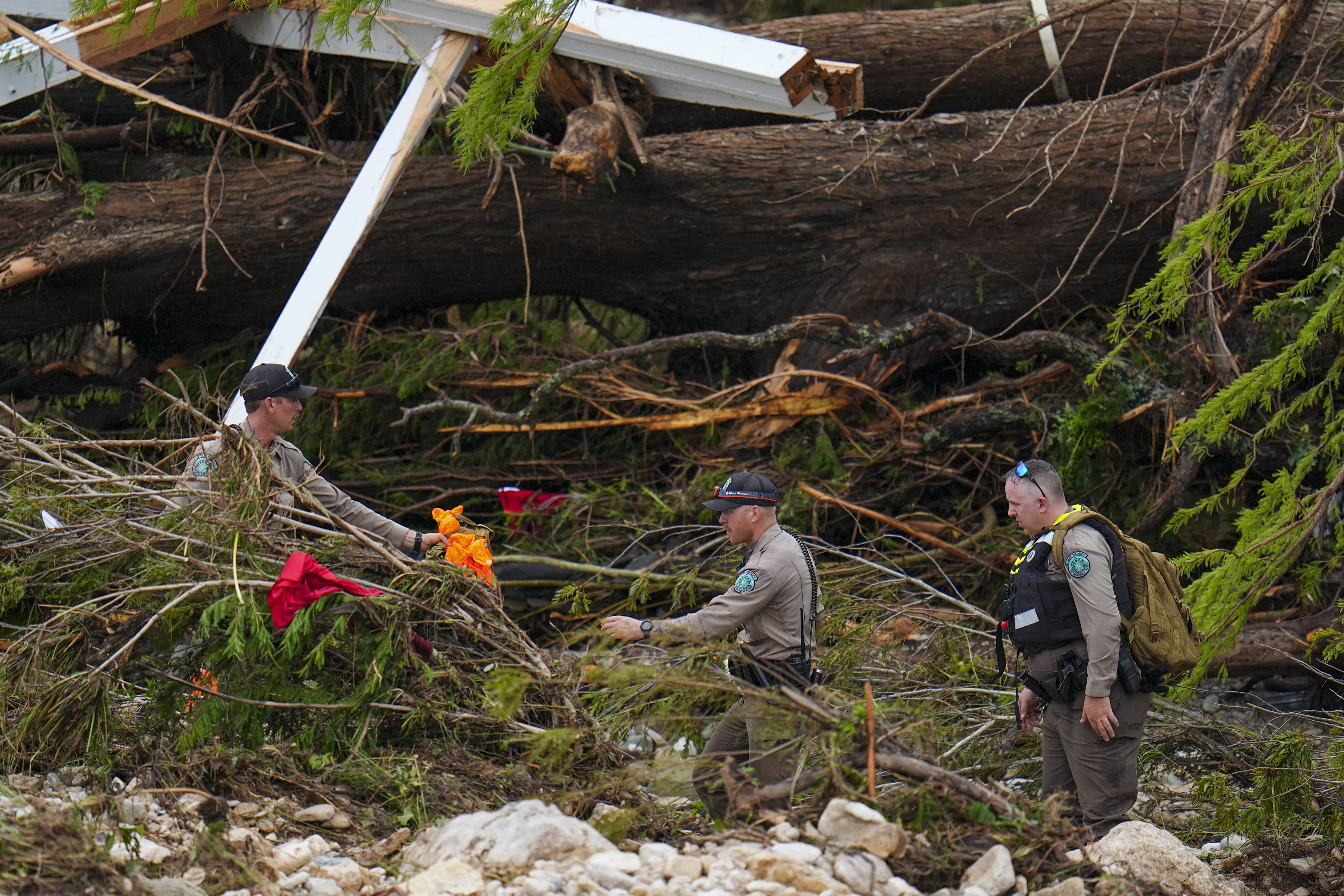 Officials with the Texas Game Warden comb through debris along the banks of the Guadalupe River after a flash flood swept through the area Saturday, July 5, 2025, in Hunt, Texas. (AP Photo/Julio Cortez)