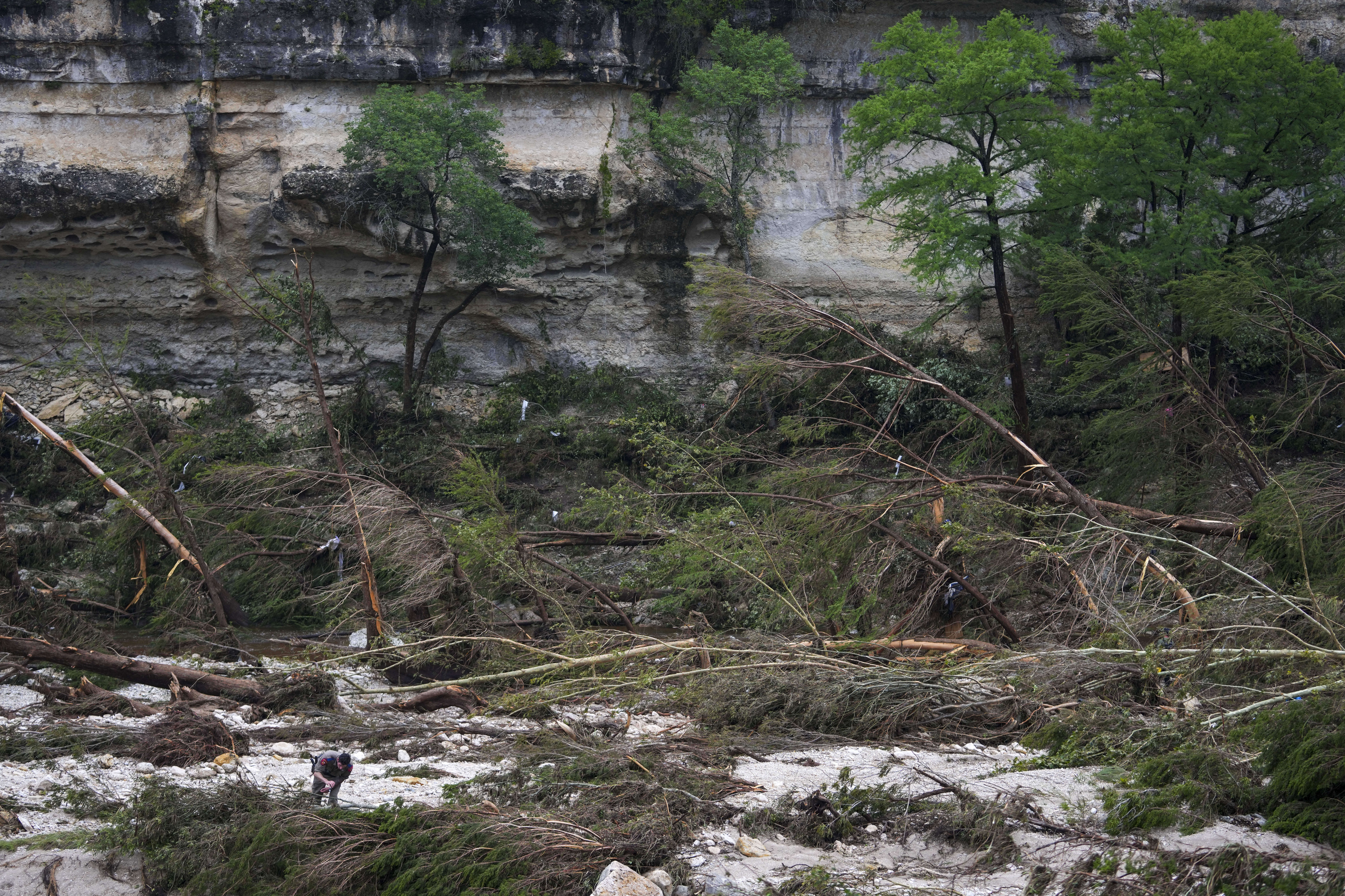 A Texas Department of Public Safety official, bottom left, combs through the banks of the Guadalupe River near Camp Mystic after a flash flood swept through the area Saturday, July 5, 2025, in Hunt, Texas. (AP Photo/Julio Cortez)