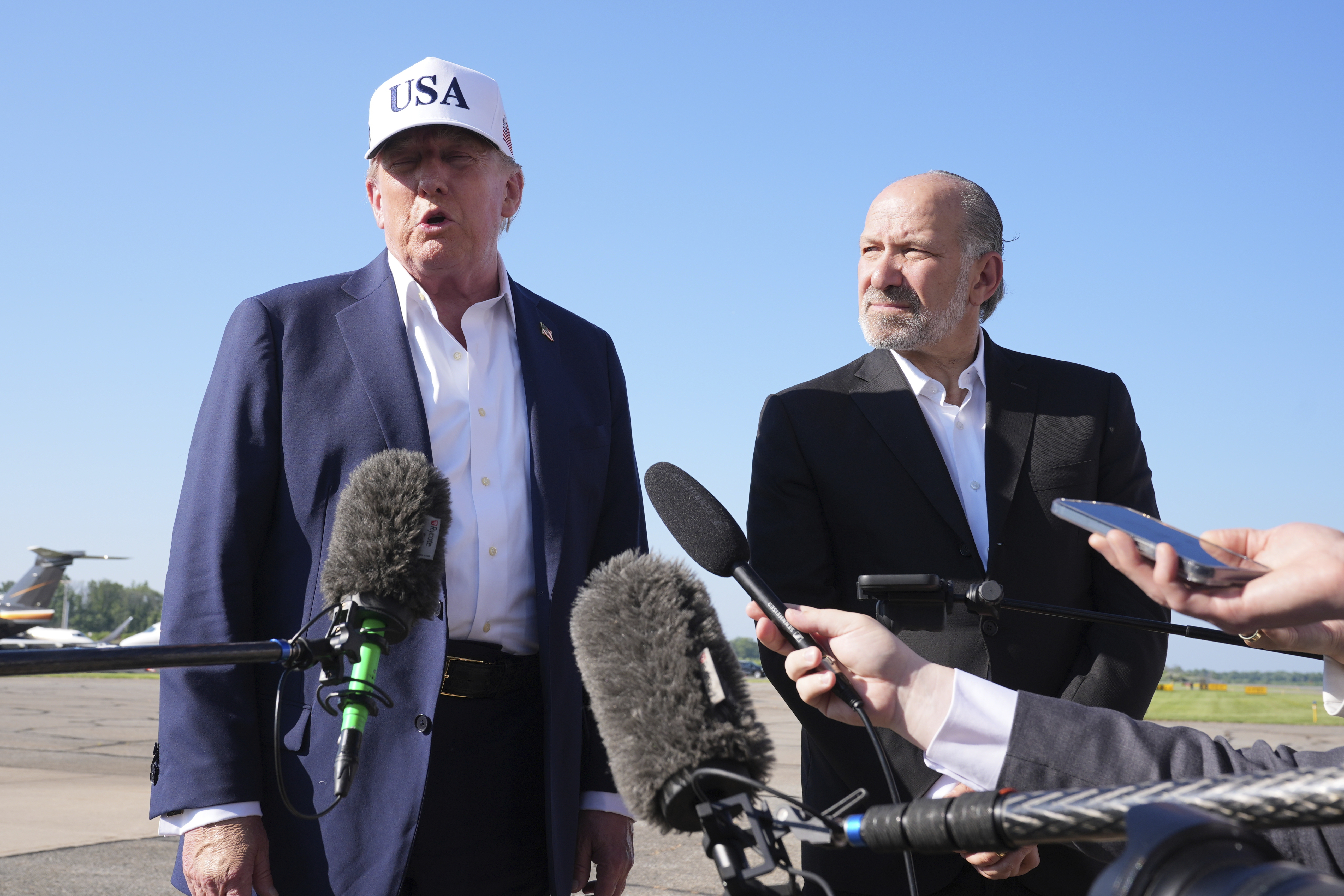 President Donald Trump, left, speaks with reporters as Commerce Secretary Howard Lutnick listens before boarding Air Force One at Morristown Municipal Airport in Morristown, N.J., Sunday, July 6, 2025, en route to Washington. (AP Photo/Jacquelyn Martin)