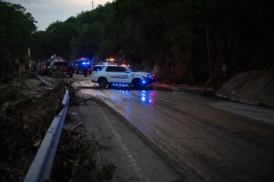Law enforcement officials block a road along the Guadalupe River as they load an extricated body into the back of a pickup truck in Hunt, Texas, Monday, July 7, 2025, after a flash flood swept through the area. (AP Photo/Eli Hartman)