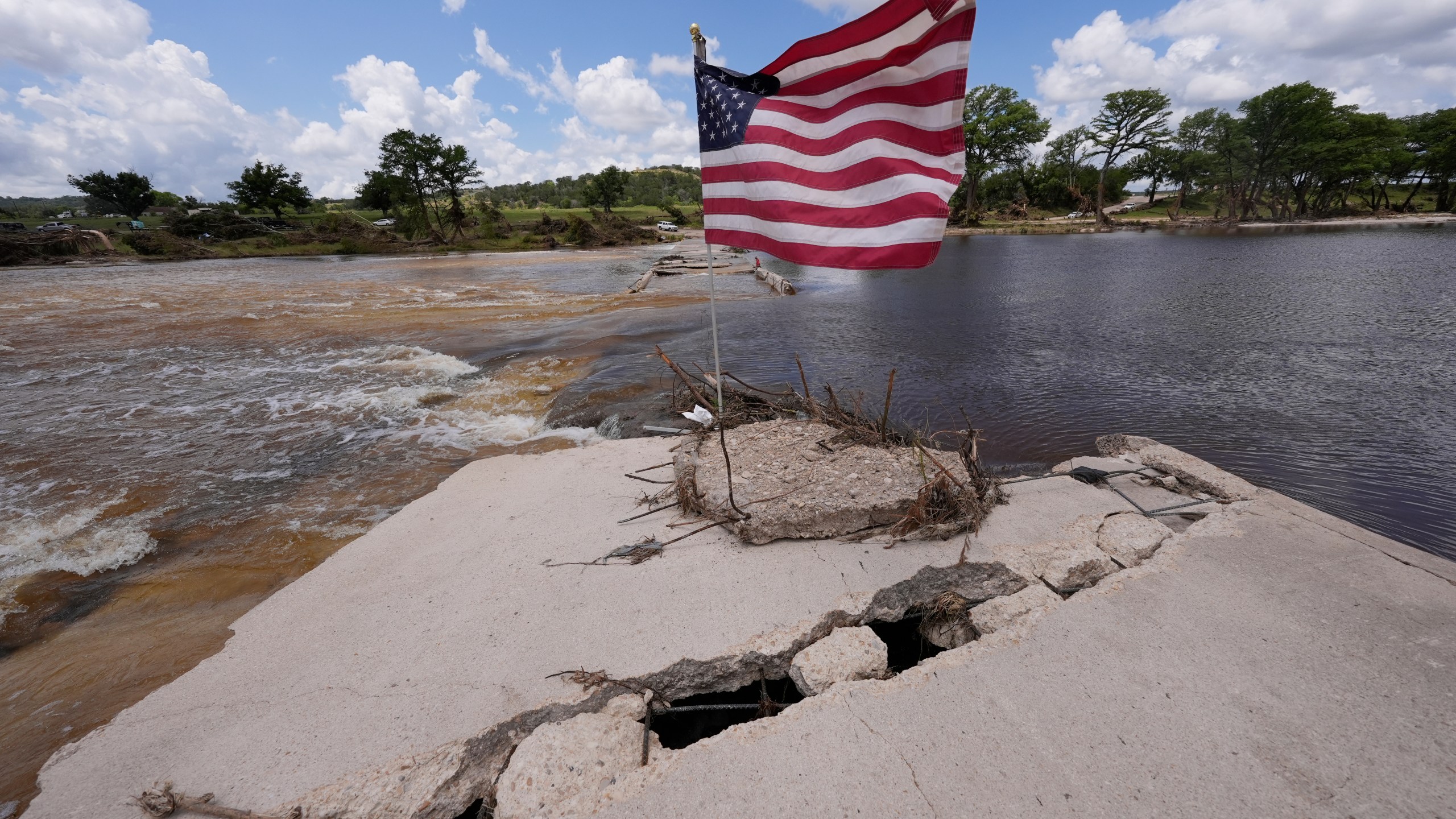 An American flag sits on a destroyed bridge over the Guadalupe River at Arcadia Loop and Bear Creek Road after flooding in Kerrville, Texas on Wednesday , July 9, 2025. (AP Photo/Gerald Herbert)