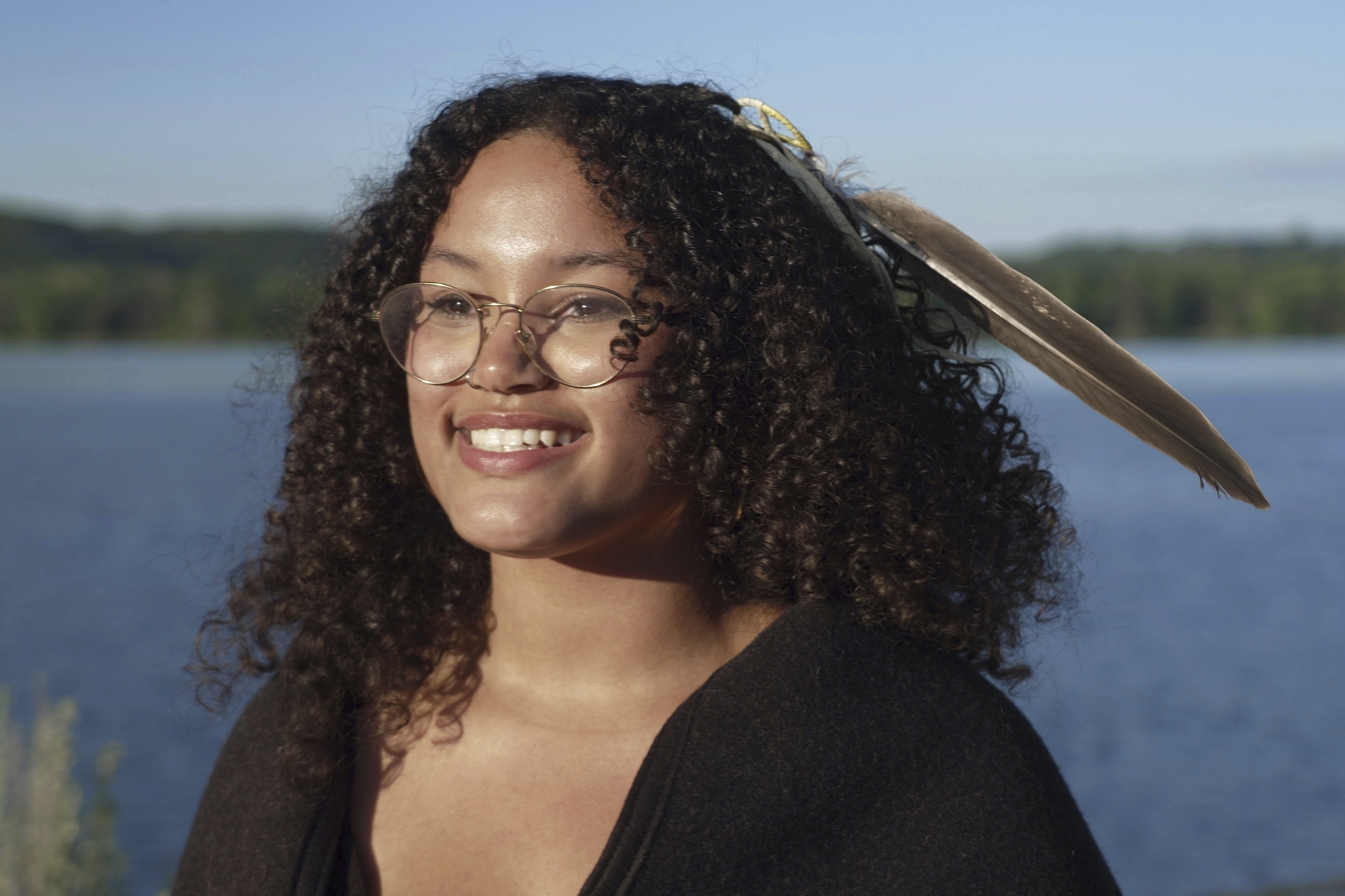 Jayvionna Buck poses for a portrait by the Mississippi River with the new bald eagle feather she received at a ceremony honoring high school graduates like her at the Prairie Island Indian Community in Minnesota on Wednesday, July 9, 2025. (AP Photo/Mark Vancleave)