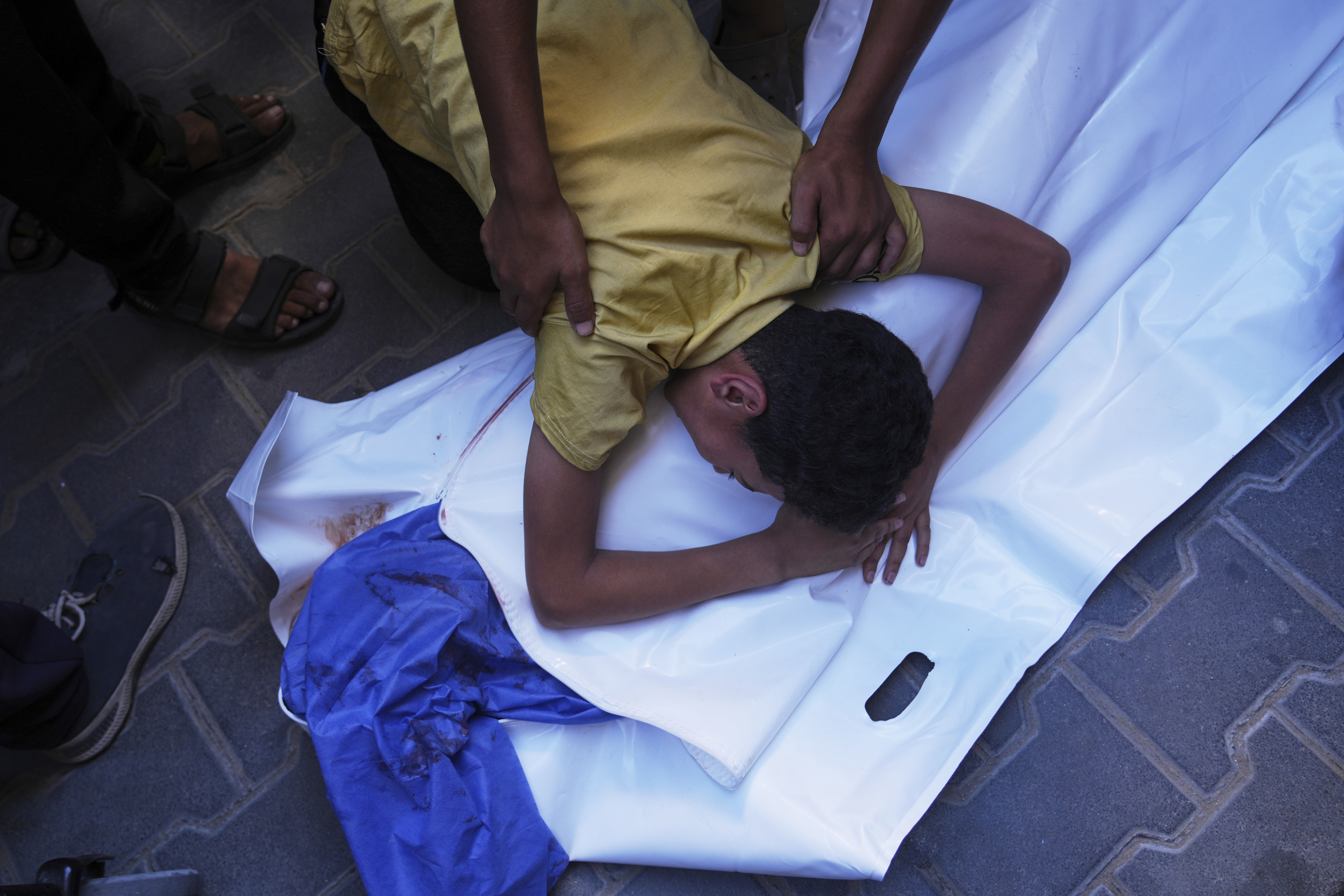 A Palestinian boy mourns over the body of his 12-year-old friend, Abdullah Ahmed, who was killed in an Israeli strike that targeted a drinking water distribution point, at Al-Awda Hospital in Nuseirat, central Gaza Strip, Sunday, July 13, 2025. (AP Photo/Abdel Kareem Hana)