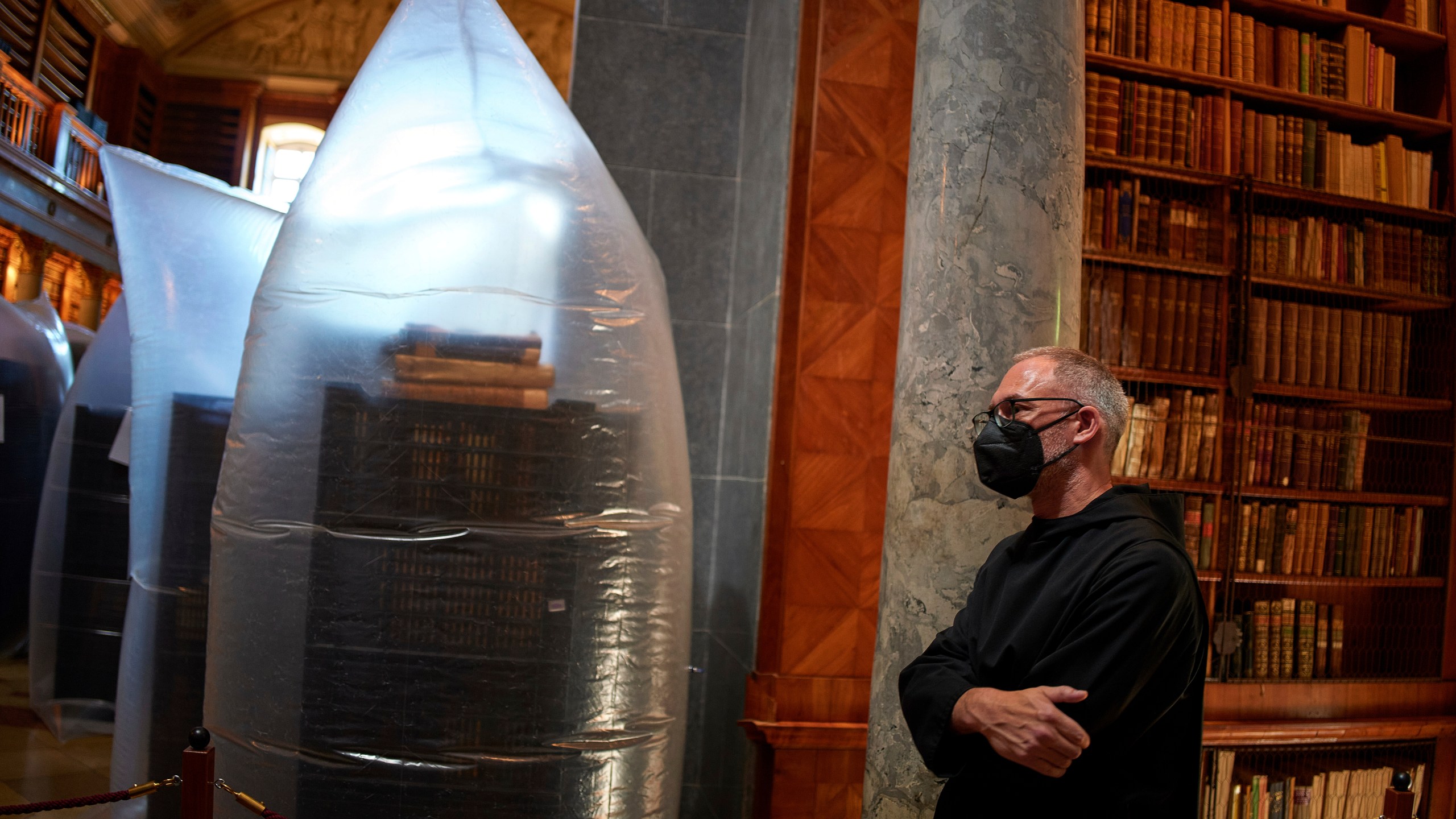 A priest wearing a face mask stands by books kept in hermetically sealed plastic sacks for disinfection at the Pannonhalma Archabbey's library in Pannonhalma, Hungary, Thursday, July 3, 2025, as a beetle infestation threatens its ancient collection. (AP Photo/Bela Szandelszky)