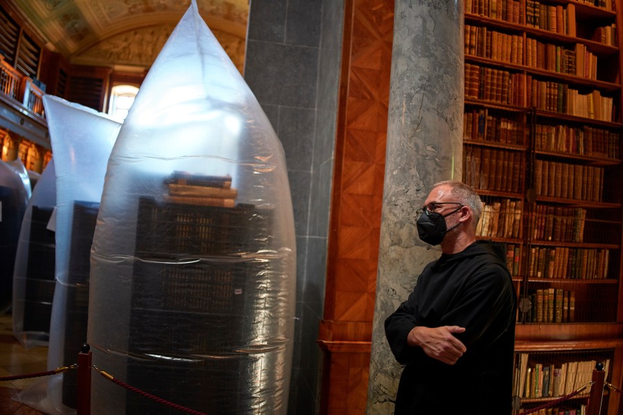 A priest wearing a face mask stands by books kept in hermetically sealed plastic sacks for disinfection at the Pannonhalma Archabbey's library in Pannonhalma, Hungary, Thursday, July 3, 2025, as a beetle infestation threatens its ancient collection. (AP Photo/Bela Szandelszky)