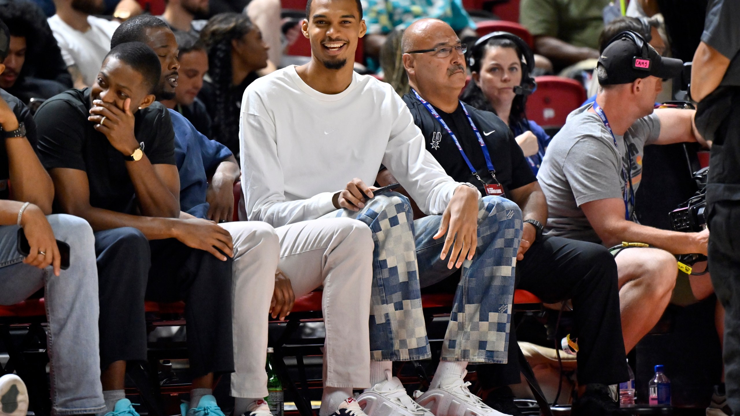San Antonio Spurs' Victor Wembanyama, center, sits court side during the first half of an NBA summer league basketball game between the Spurs and Philadelphia 76ers, Thursday, July 10, 2025, in Las Vegas. (AP Photo/David Becker)