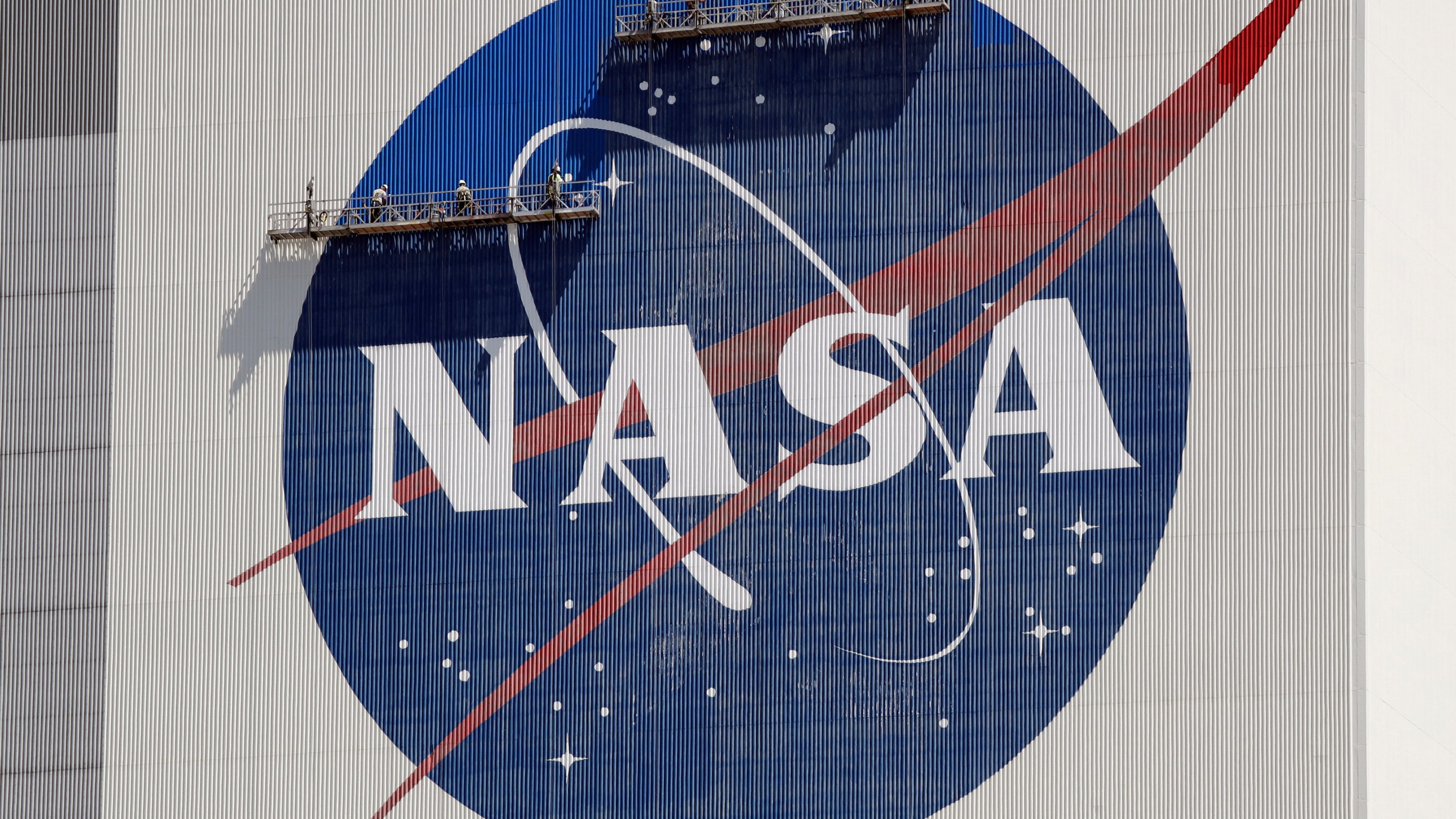 FILE - Workers on scaffolding repaint the NASA logo near the top of the Vehicle Assembly Building at the Kennedy Space Center in Cape Canaveral, Fla., May 20, 2020. (AP Photo/John Raoux, File)