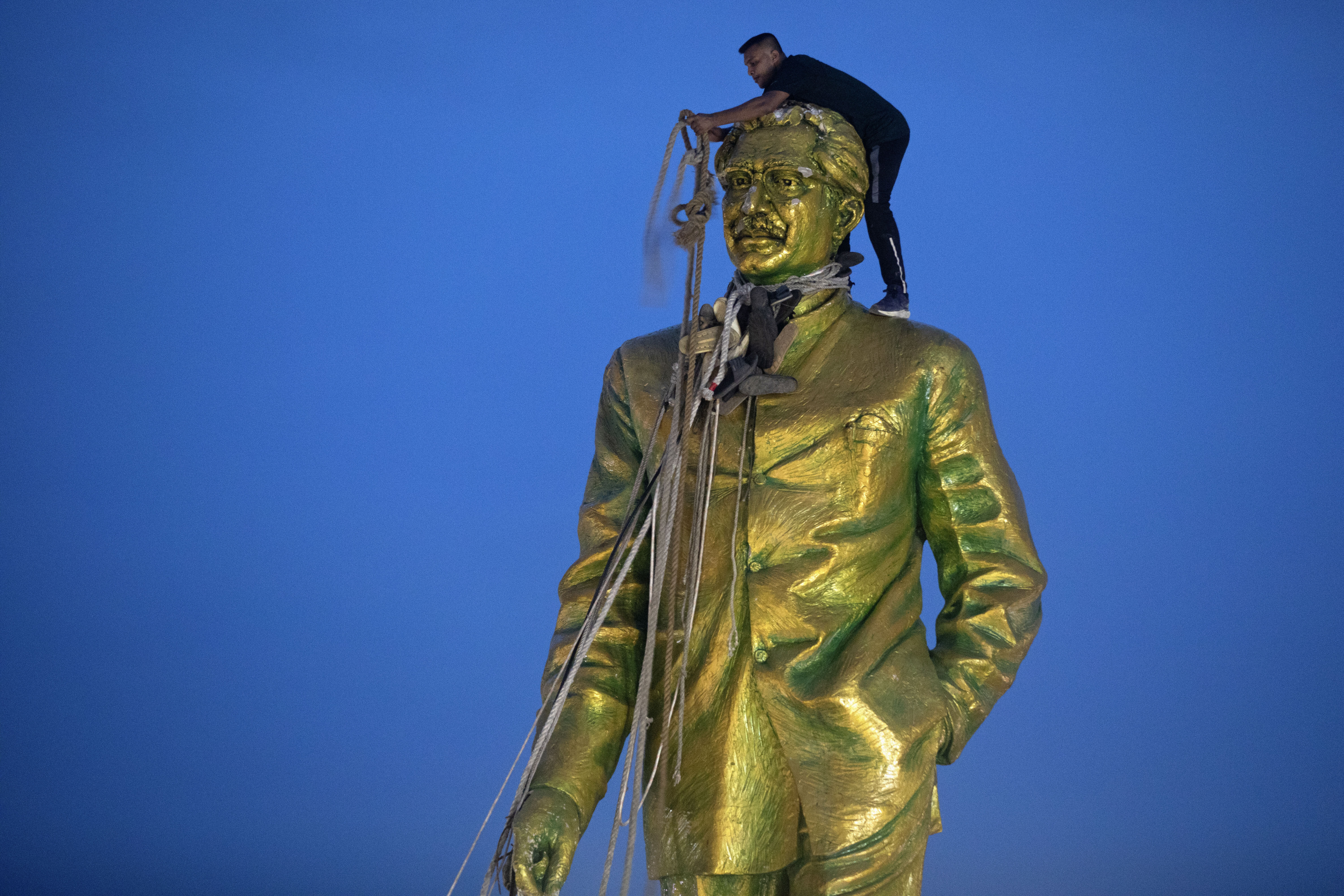 FILE - A man climbs to tie a rope around the head of a large statue of Sheikh Mujibur Rahman, father of Bangladesh leader Sheikh Hasina, as protesters try to bring it down after she resigned as Prime Minister, in Dhaka, Bangladesh, on Aug. 5, 2024. (AP Photo/Rajib Dhar, File)