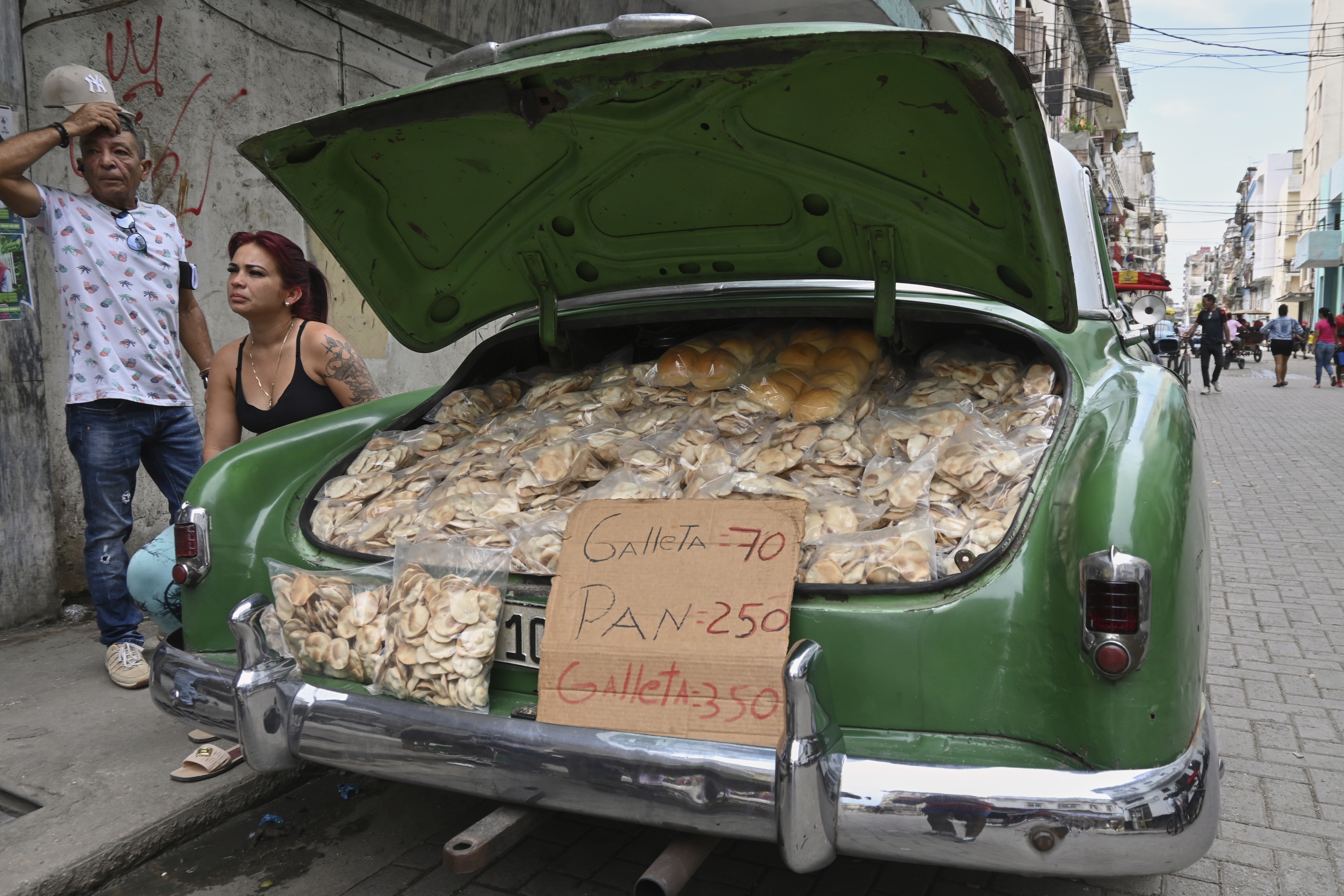 Vendors wait for customers next to the trunk of their American classic car stuffed with homemade crisps and bread, in Havana, Cuba, Tuesday, July 15, 2025. (AP Photo/Jorge Luis Baños)