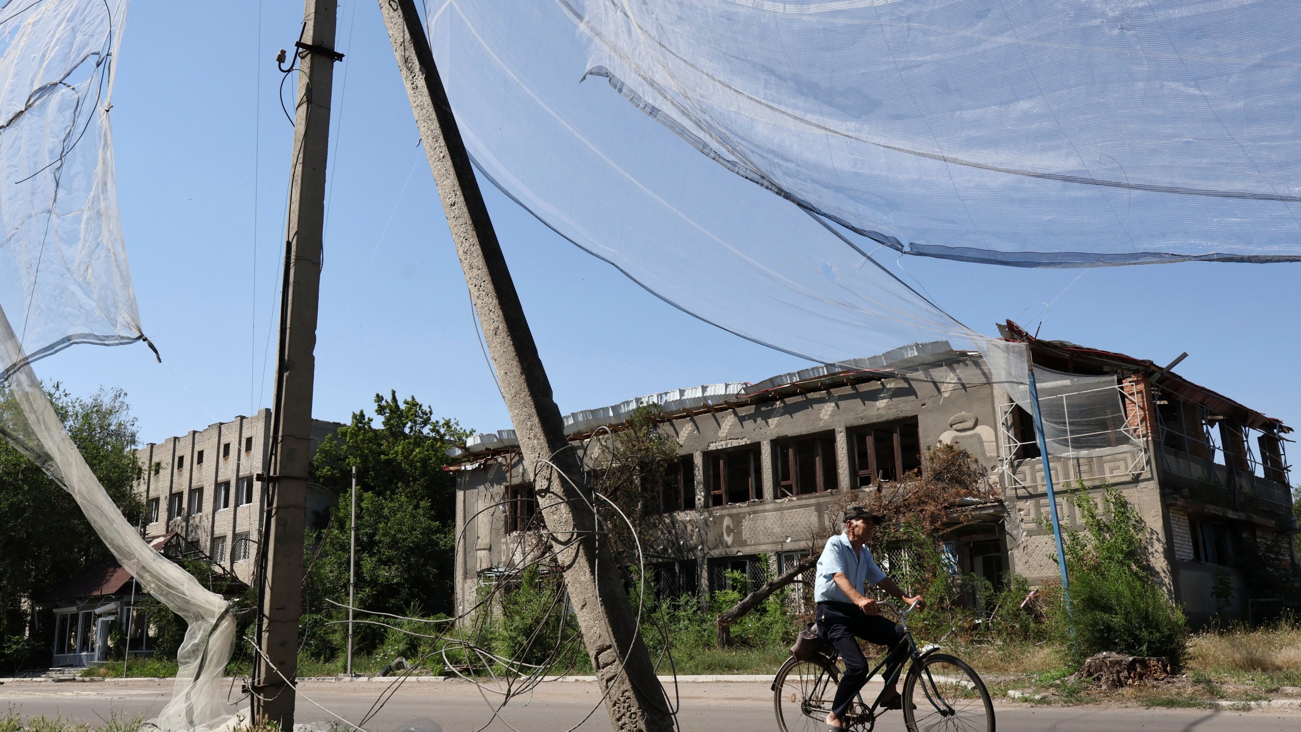 In this photo provided by Ukraine's 65th Mechanized Brigade press service, a local resident rides a bike along the street under an anti-drone net in Orikhiv, Zaporizhzhia region, Ukraine, Tuesday, July 15, 2025. (Andriy Andriyenko/Ukraine's 65th Mechanized Brigade via AP)