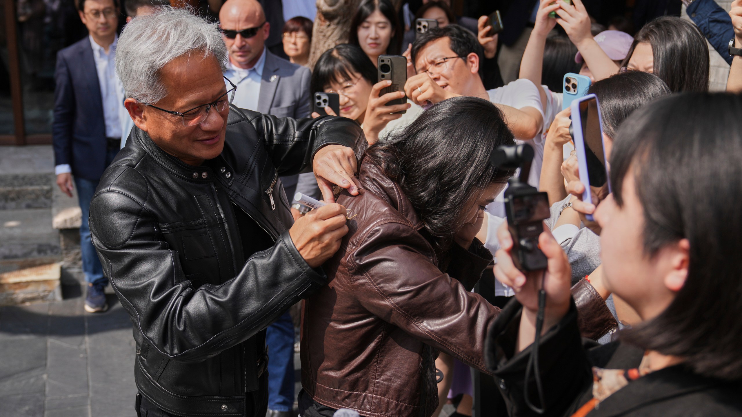 CEO of Nvidia Jensen Huang gives an autograph on a leather jacket of a reporter as he arrives for a press conference at the Mandarin Oriental Qianmen after attending the third China International Supply Chain Expo, in Beijing, Wednesday, July 16, 2025. (AP Photo/Andy Wong)