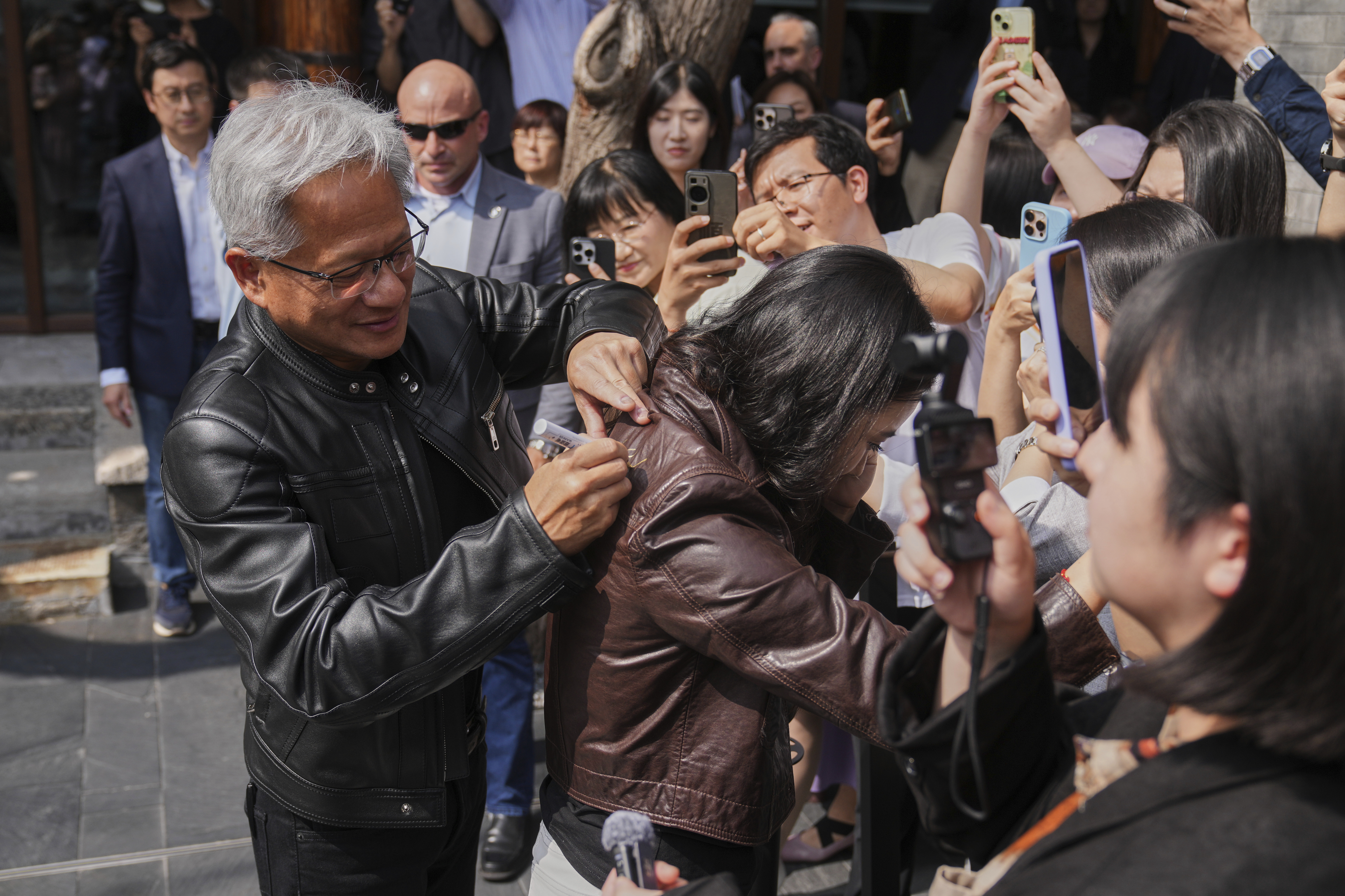 CEO of Nvidia Jensen Huang gives an autograph on a leather jacket of a reporter as he arrives for a press conference at the Mandarin Oriental Qianmen after attending the third China International Supply Chain Expo, in Beijing, Wednesday, July 16, 2025. (AP Photo/Andy Wong)
