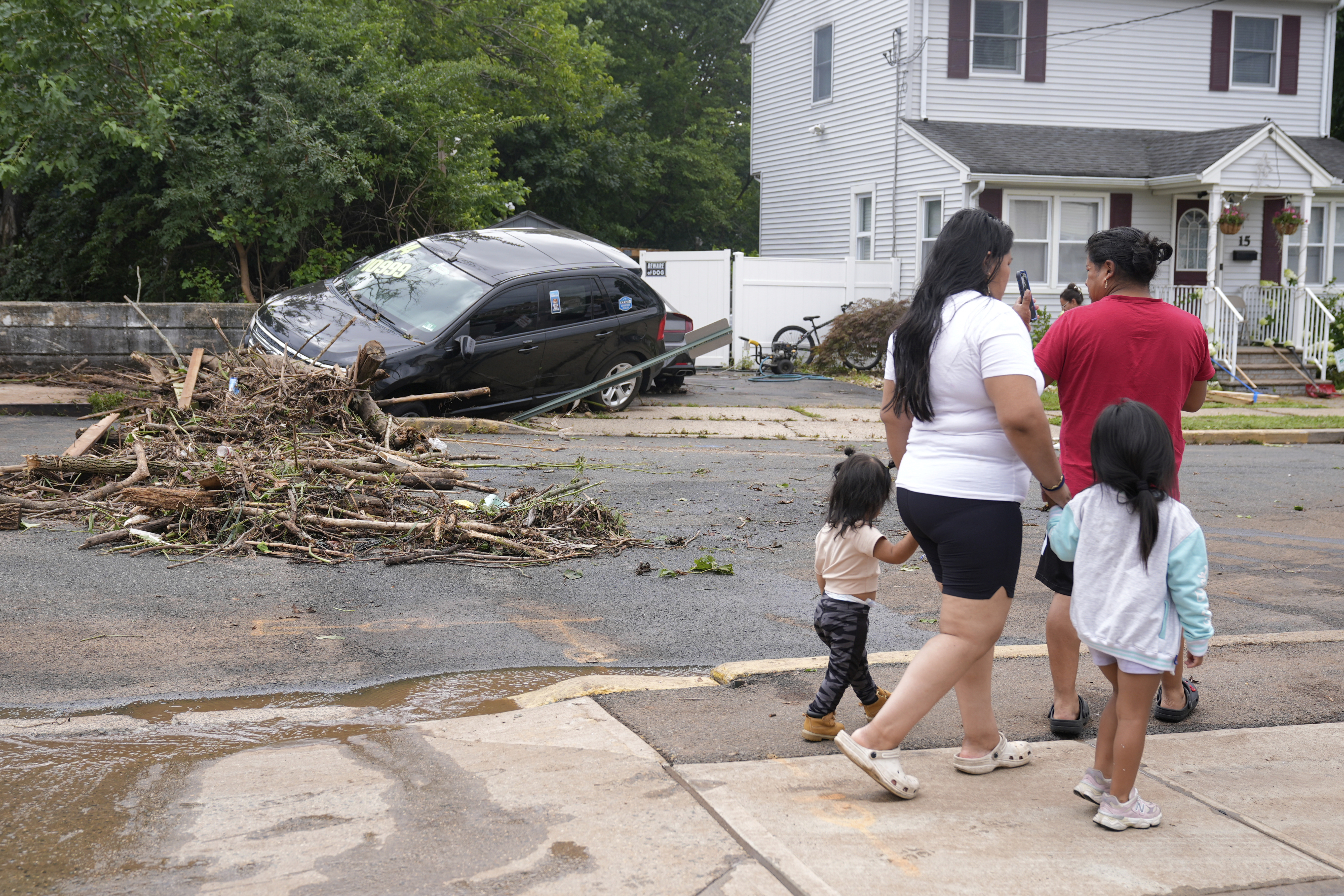 A family walks by flood-damaged cars in North Plainfield, N.J., Tuesday, July 15, 2025. (AP Photo/Seth Wenig)