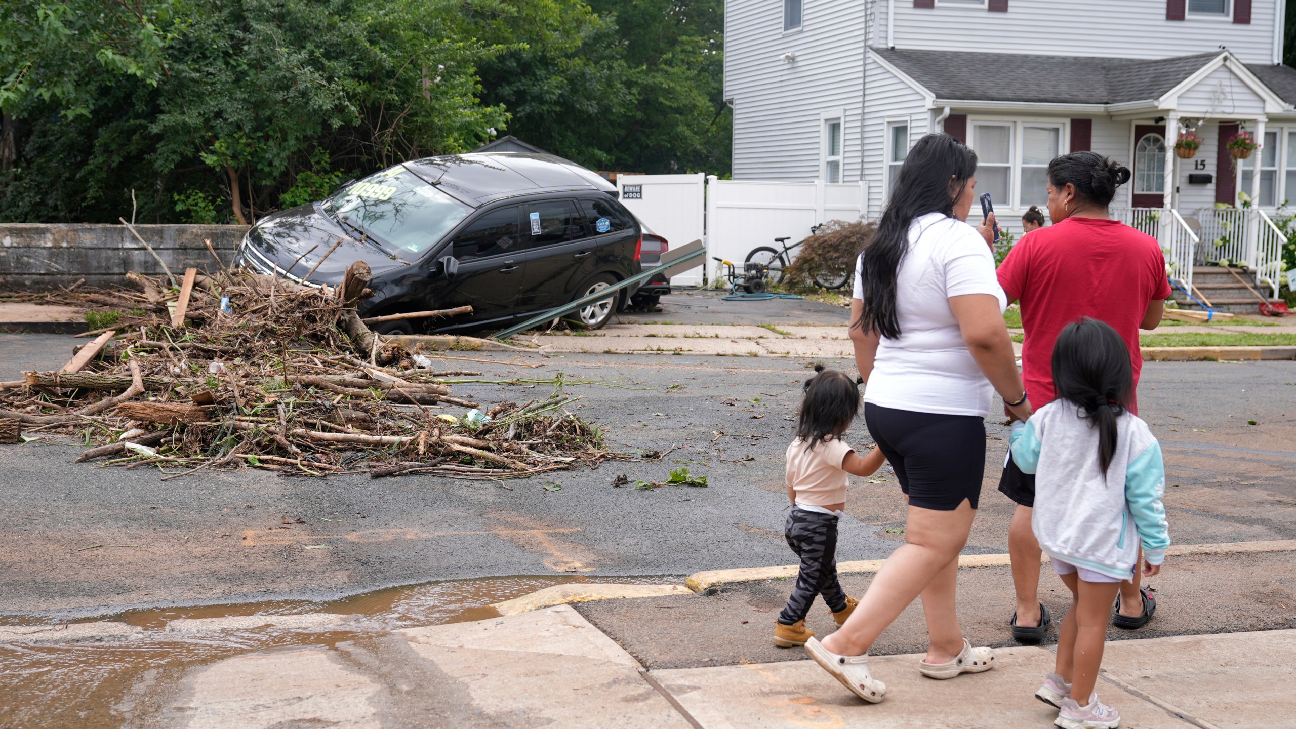 A family walks by flood-damaged cars in North Plainfield, N.J., Tuesday, July 15, 2025. (AP Photo/Seth Wenig)