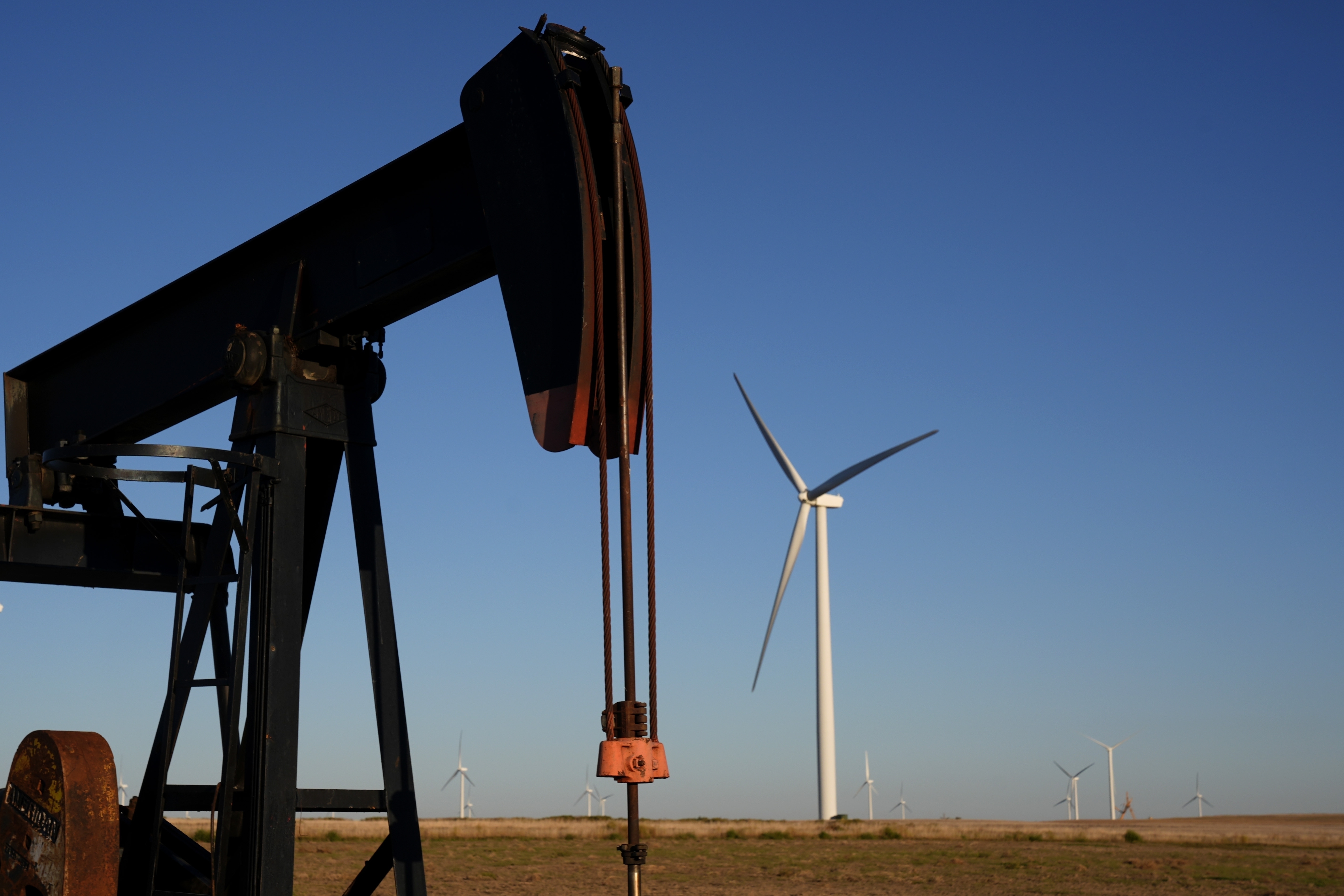 FILE - Pumpjacks operate in the foreground while a wind turbines at the Buckeye Wind Energy wind farm rise in the distance Monday, Sept. 30, 2024, near Hays, Kan. (AP Photo/Charlie Riedel, File)